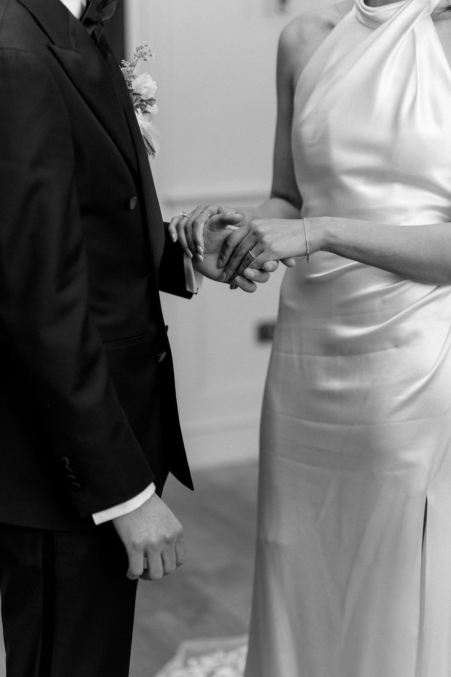Close-up black and white photo of bride and groom holding hands during wedding ceremony.