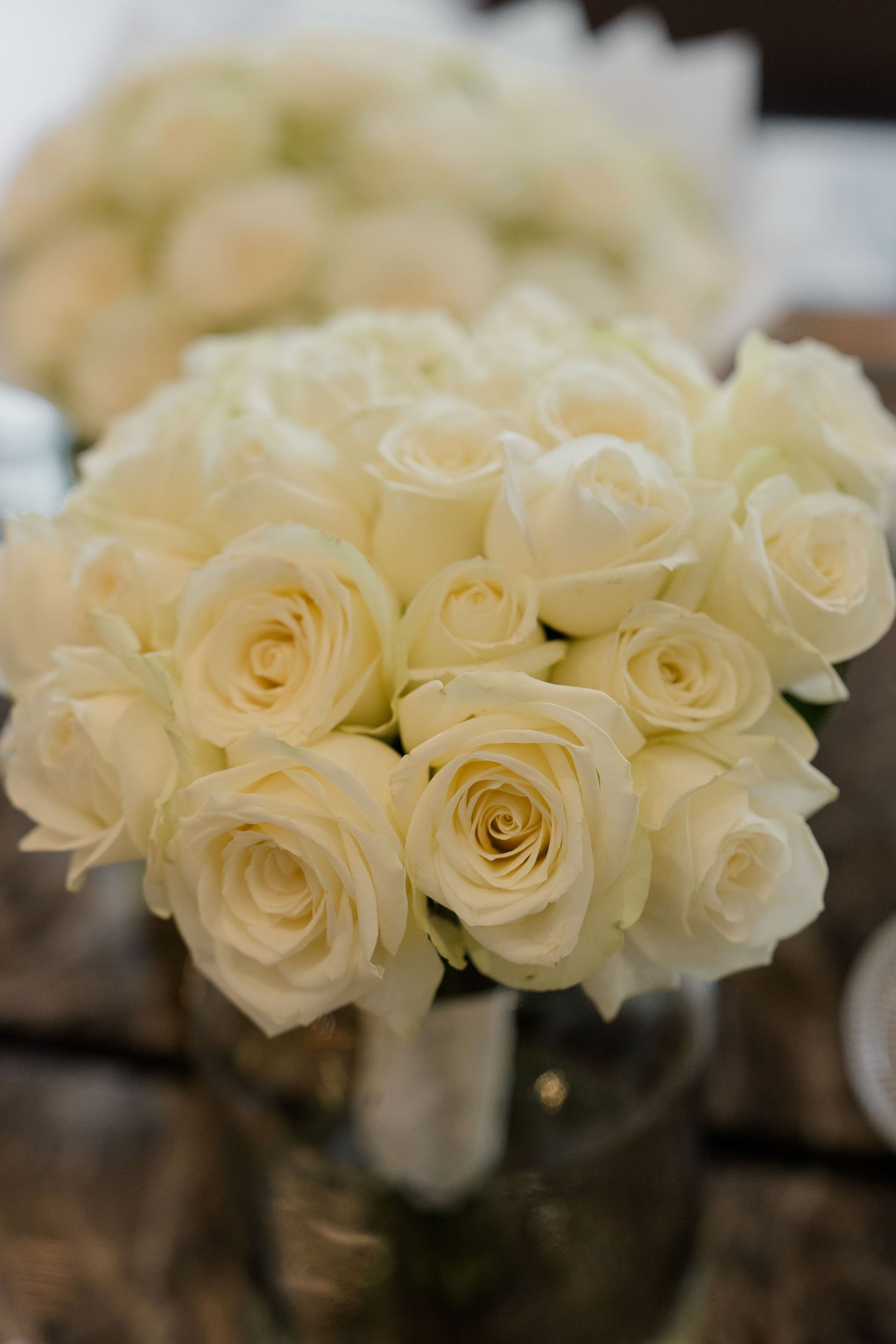 Elegant bouquet of white roses arranged in a glass vase on a wooden table, perfect for weddings.
