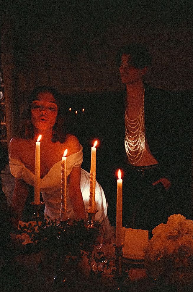 A candlelit scene with lit white candles, flowers and a beaded statue silhouetted in the dark background.