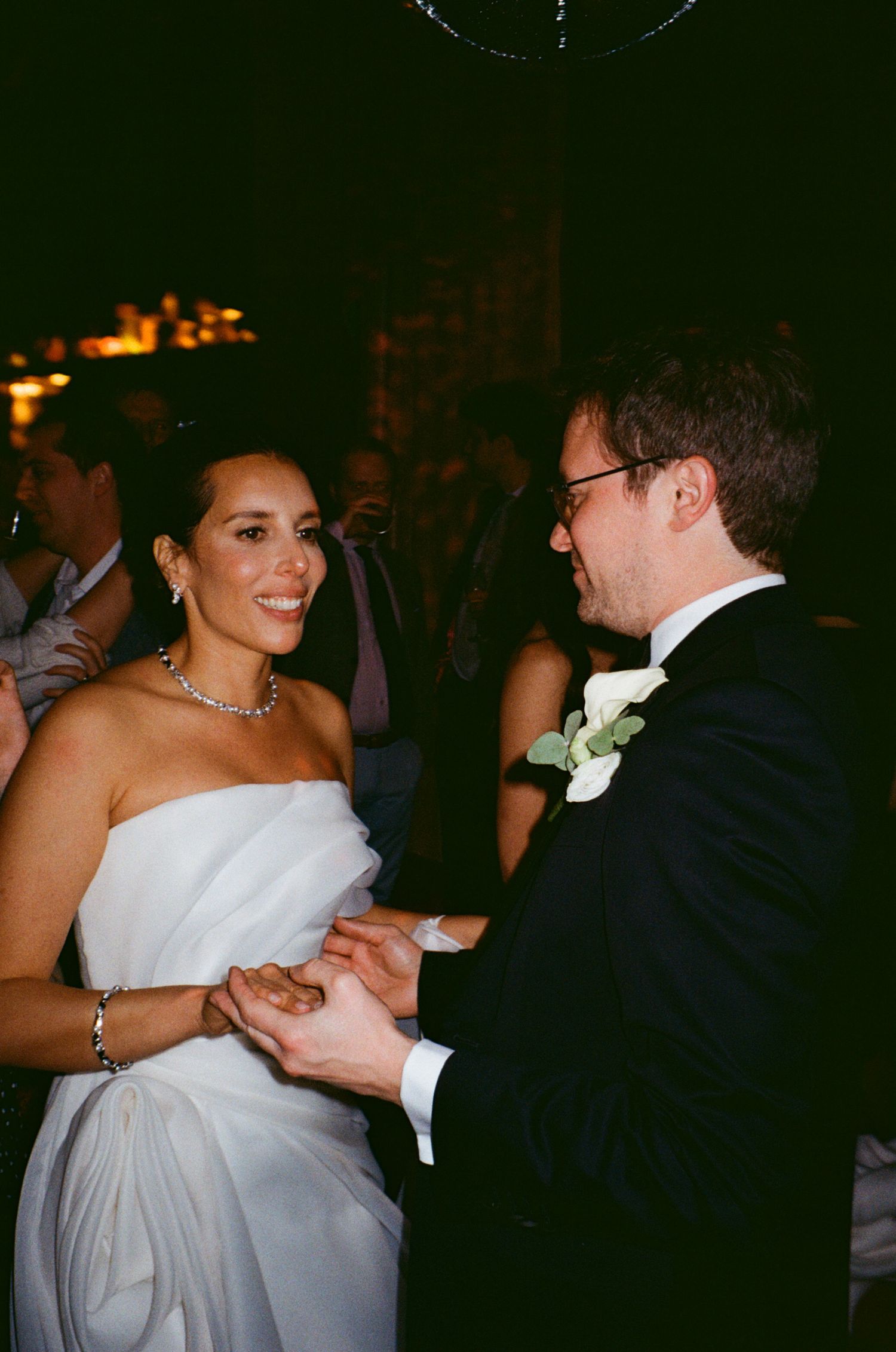A couple dances together at an elegant wedding reception with the bride in a white strapless gown.