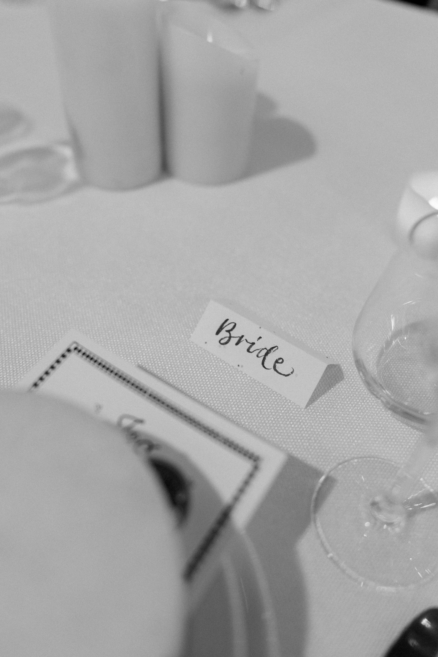 Close-up detail shot of elegant wedding place card with calligraphy on white linen tablecloth.