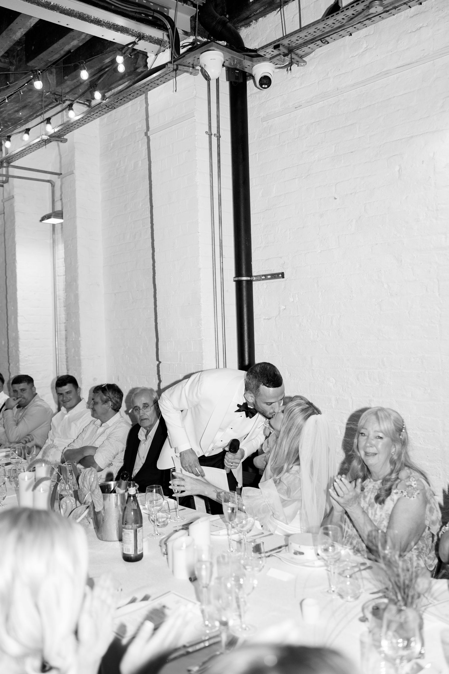 Wedding guests enjoying dinner conversation at elegant white tables with wine glasses.