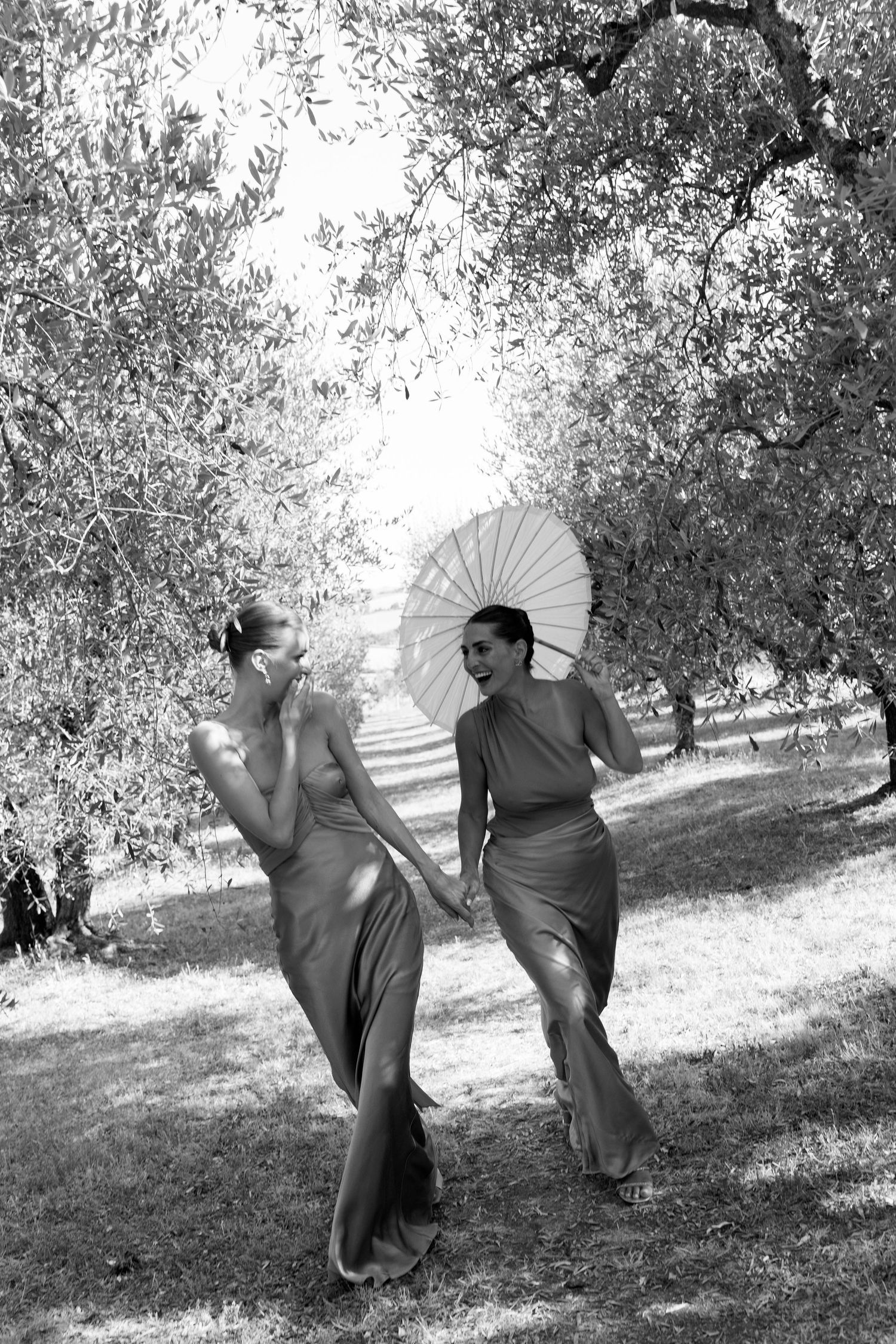 Playful dance scene with white parasols in an olive grove captured in black and white.