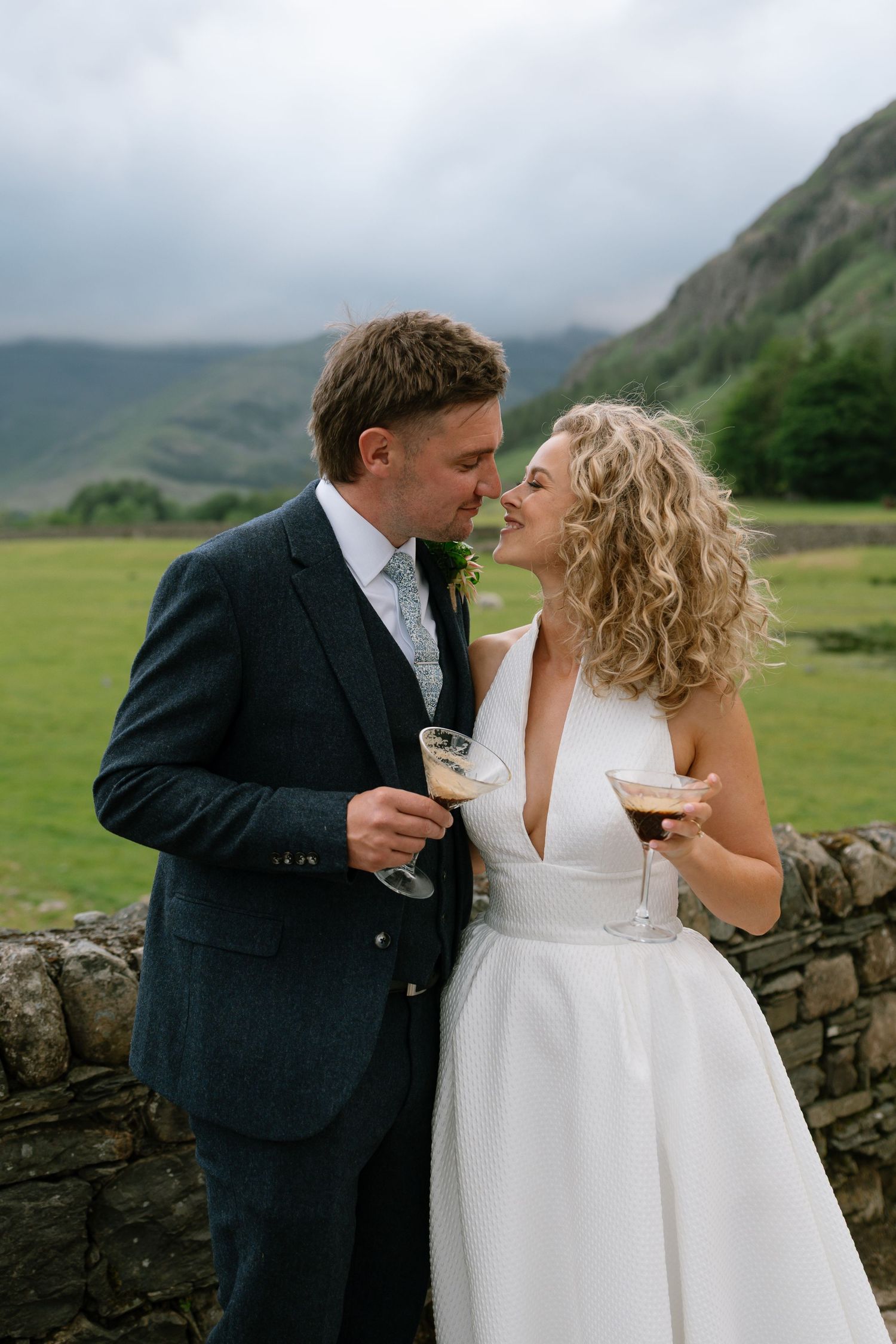 Bride and groom share champagne together in front of scenic mountain landscape.