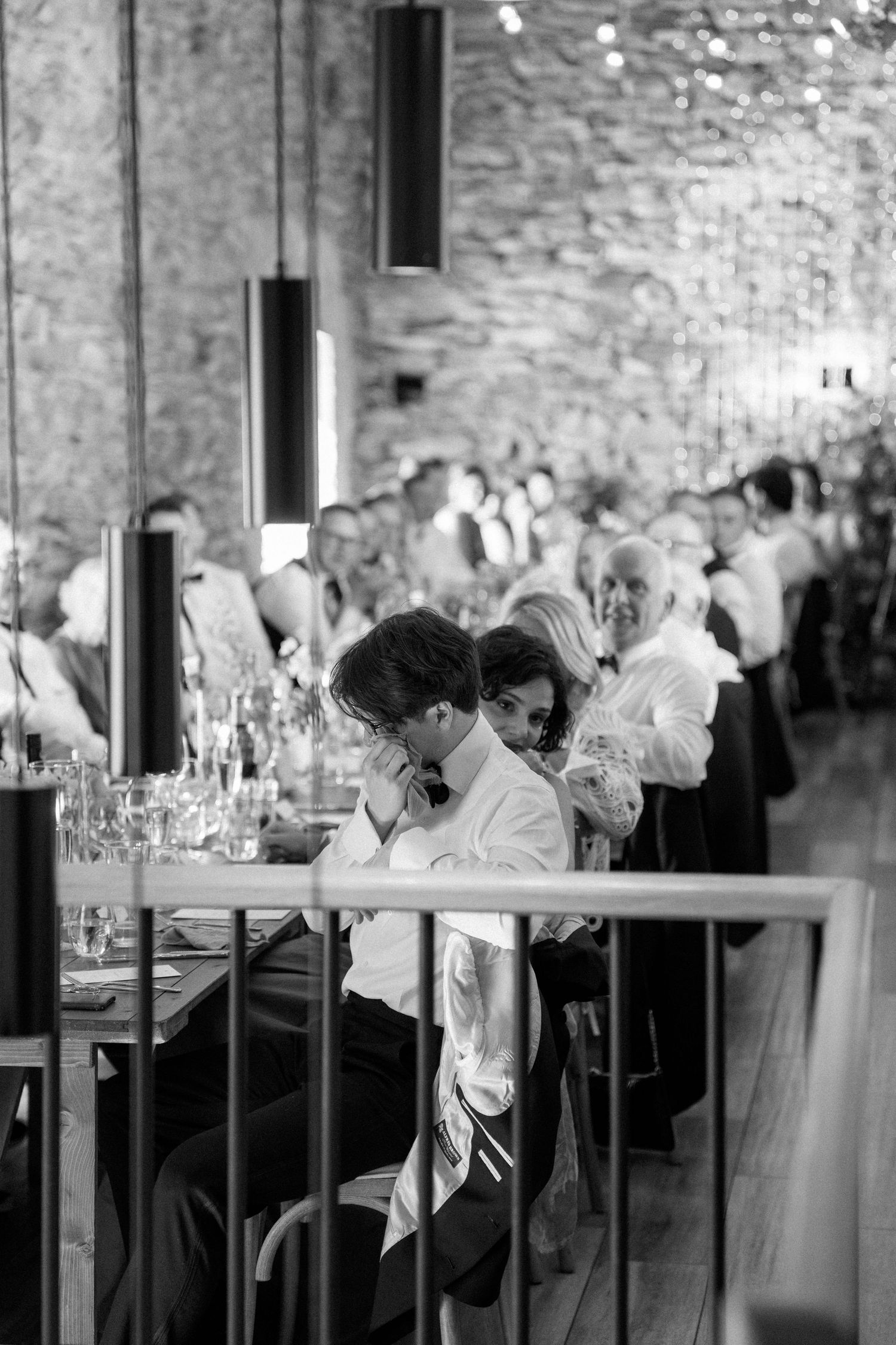 Wedding reception guests dining at long tables in a rustic stone venue with ambient lighting.