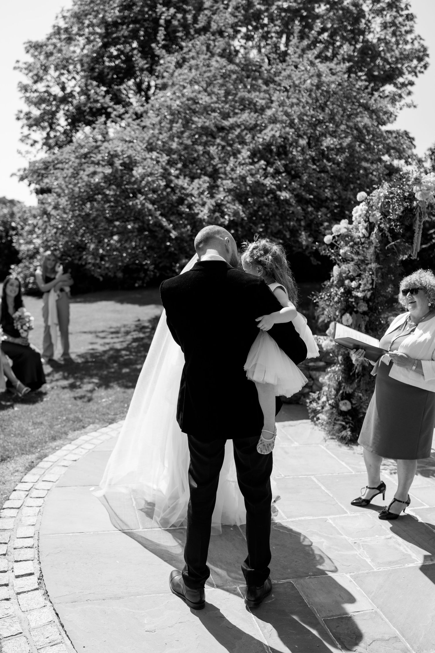 Black and white photo of couples dancing on a stone pathway at an outdoor wedding.