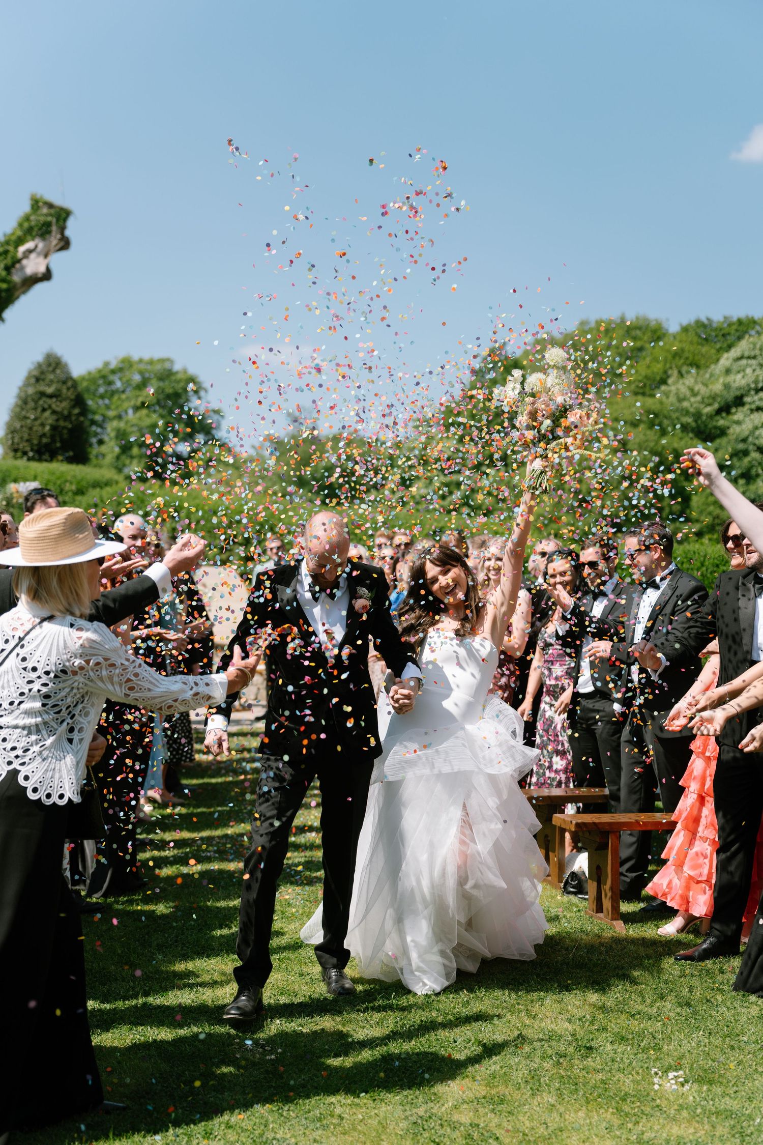 Celebratory moment as wedding party and guests toss confetti in an outdoor garden ceremony.