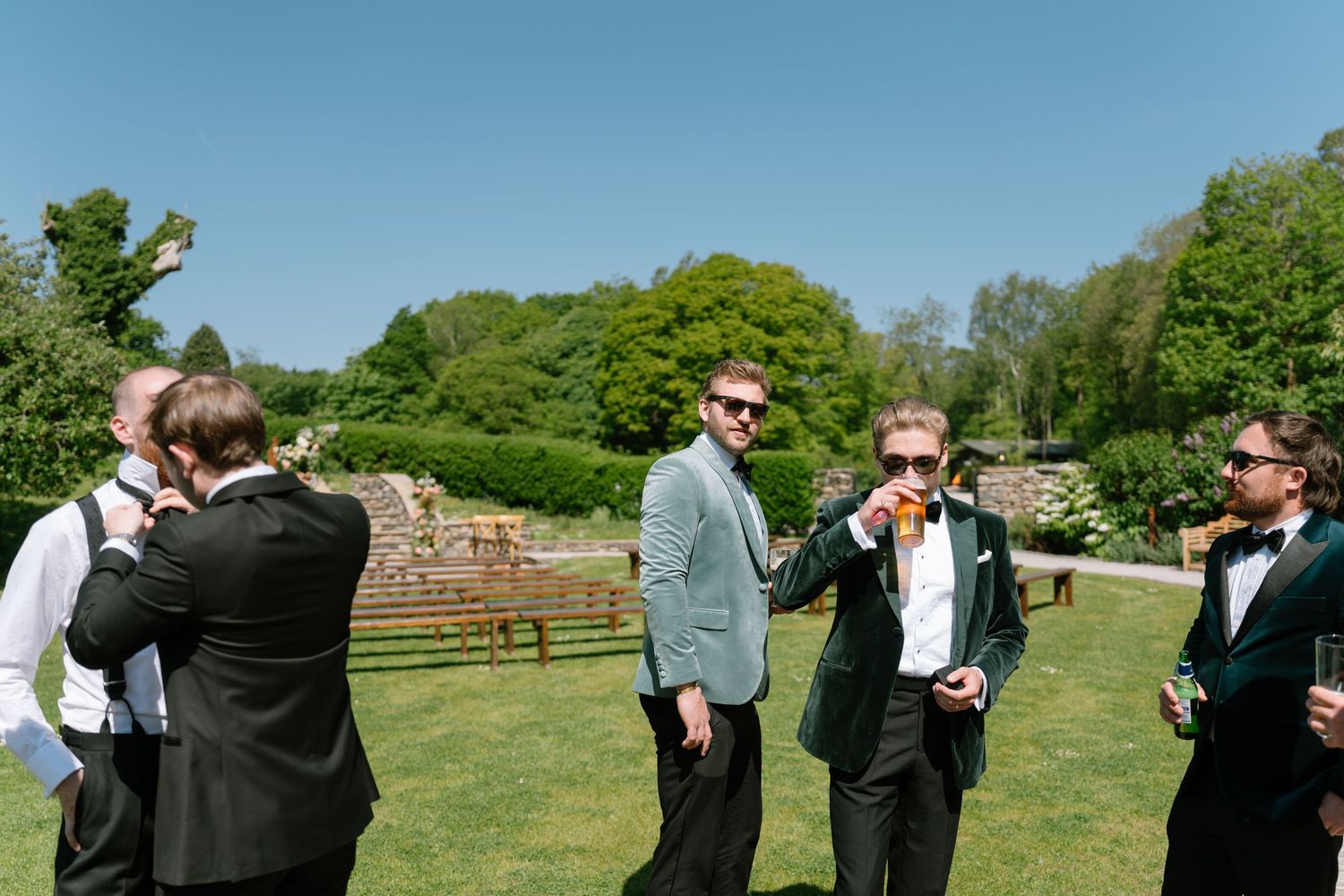 Wedding party gathered on grassy field during sunny outdoor celebration.