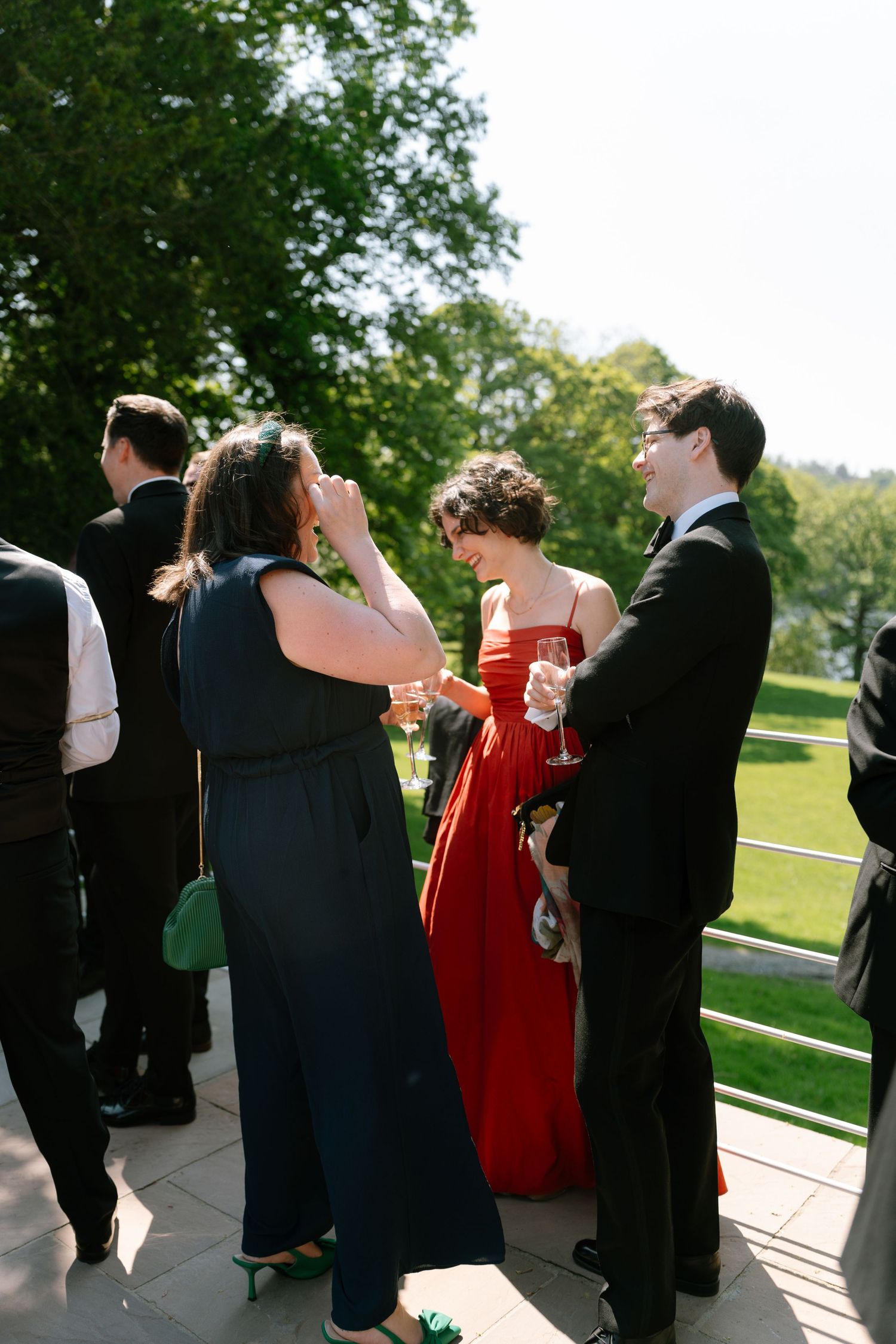 Wedding guests in formal attire mingling on an outdoor terrace.