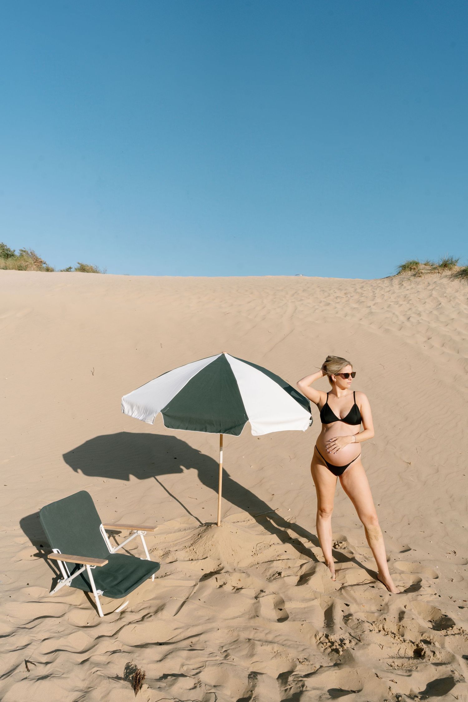 Beach scene with umbrellas and figure setting up on sand dunes.