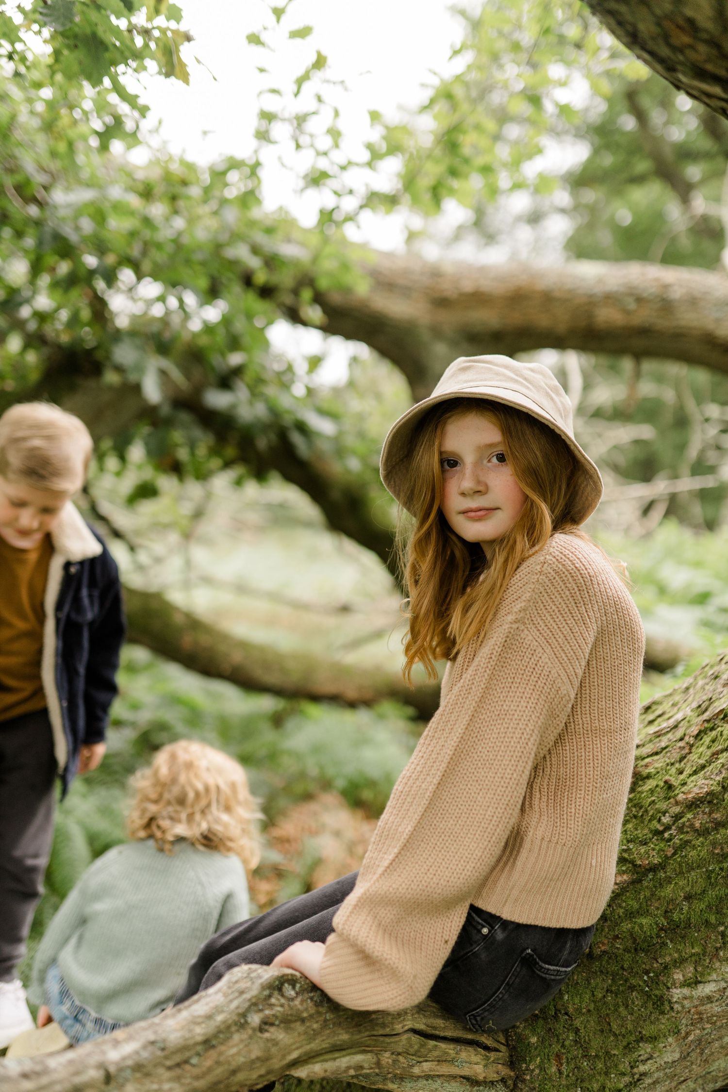 People relax on a fallen tree branch in a lush green forest setting.