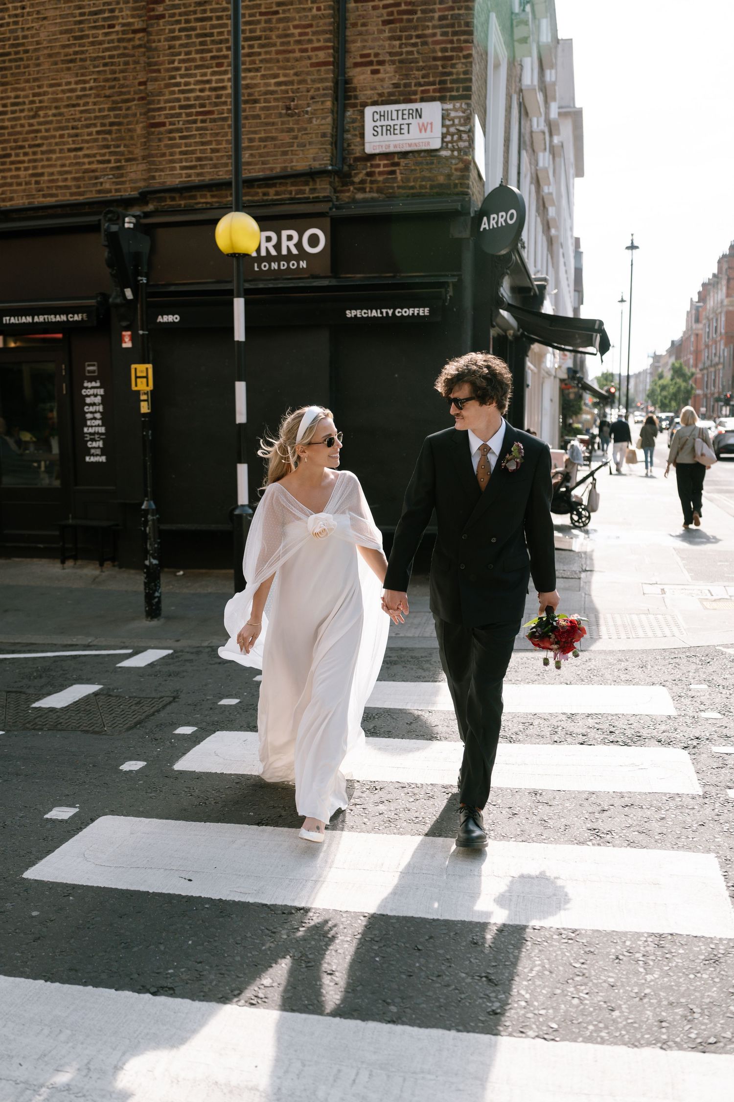 A couple crosses a zebra crossing in wedding attire near the Arro storefront.