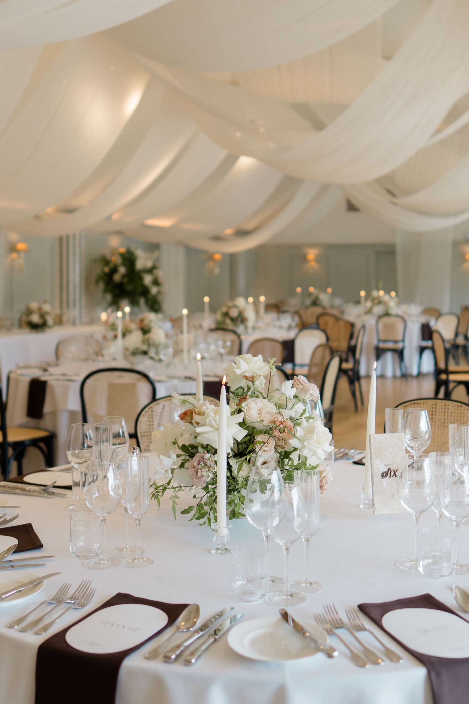 Elegant white wedding reception tent with floral centerpieces and dark ribbon napkins.