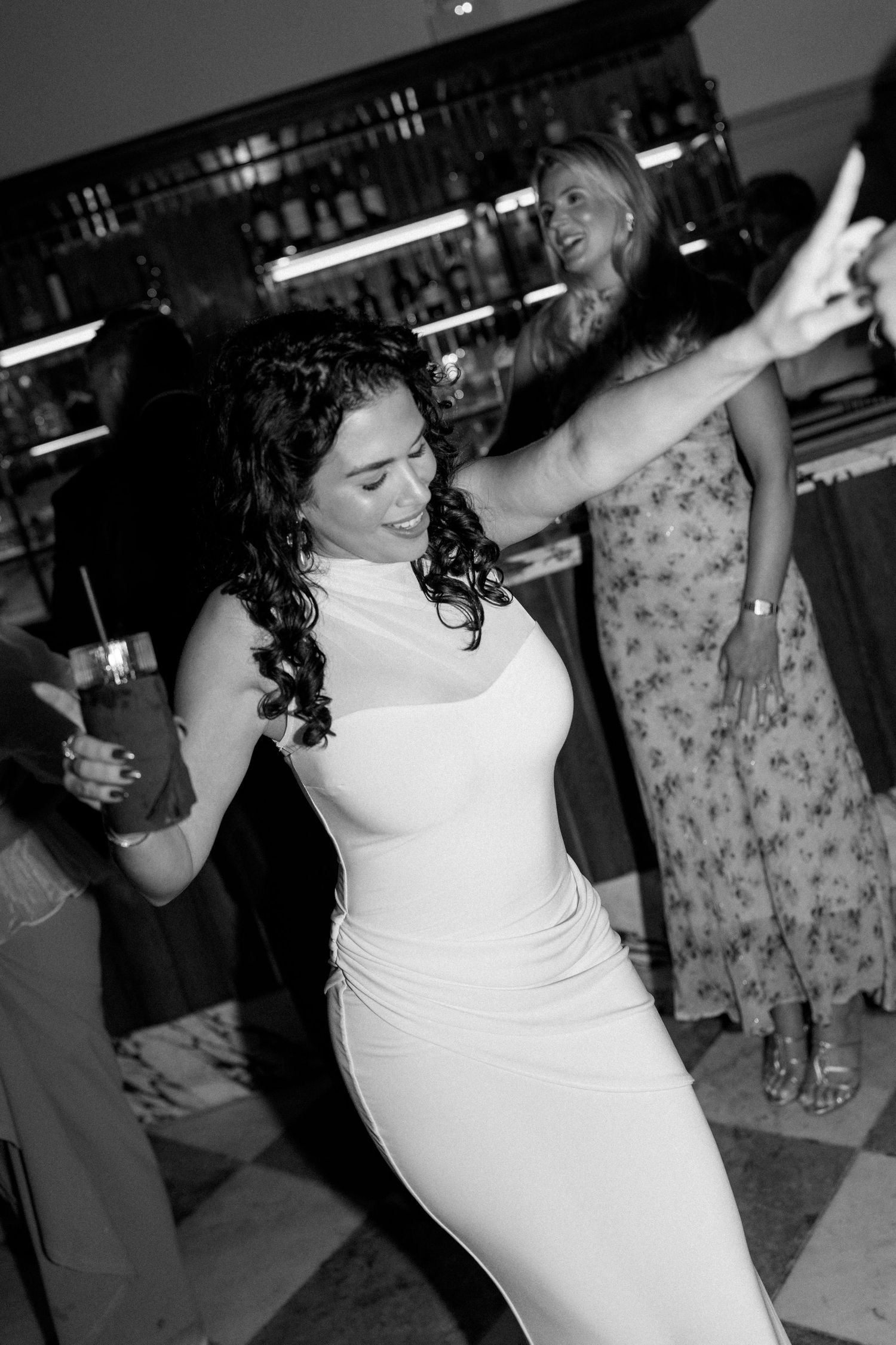 Bride in white fitted gown dancing joyfully at wedding reception in black and white photo.