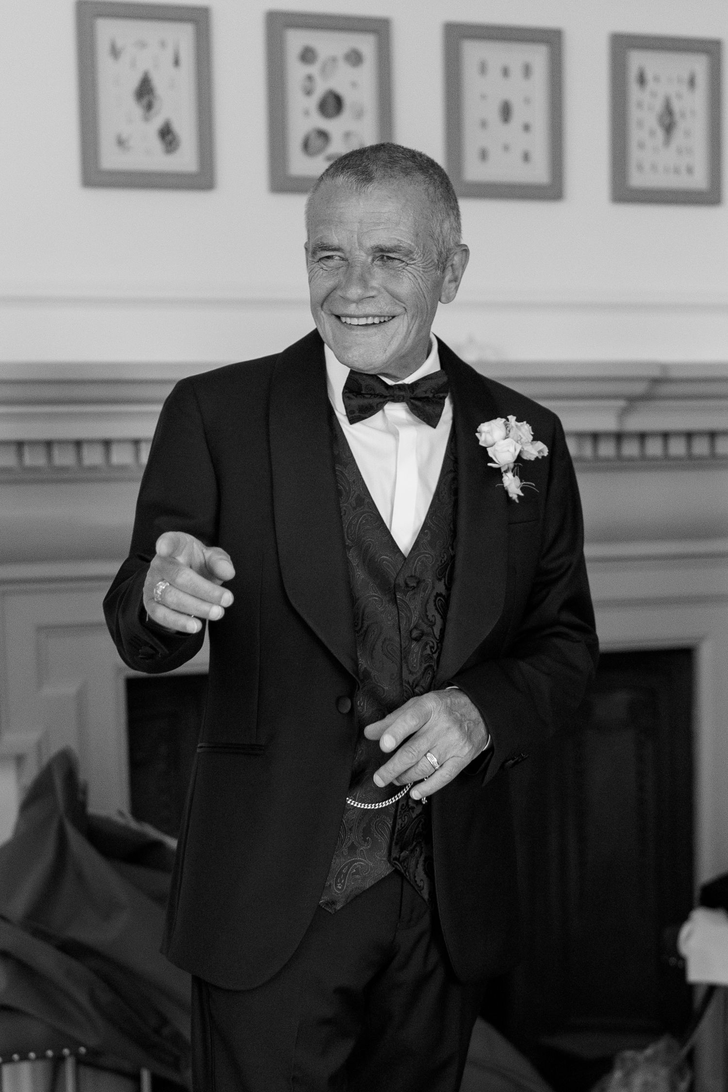 Black and white portrait of smiling older man in tuxedo with boutonniere at wedding reception.