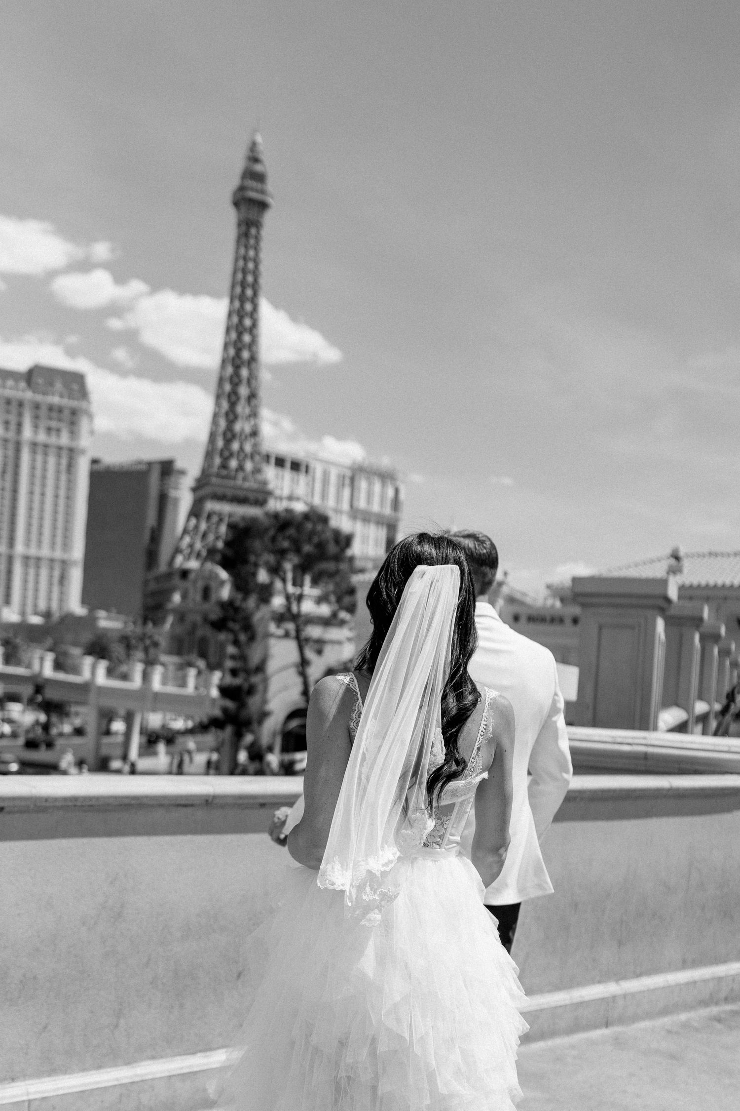 A black and white photo of newlyweds posing with the Las Vegas skyline and Eiffel Tower replica.