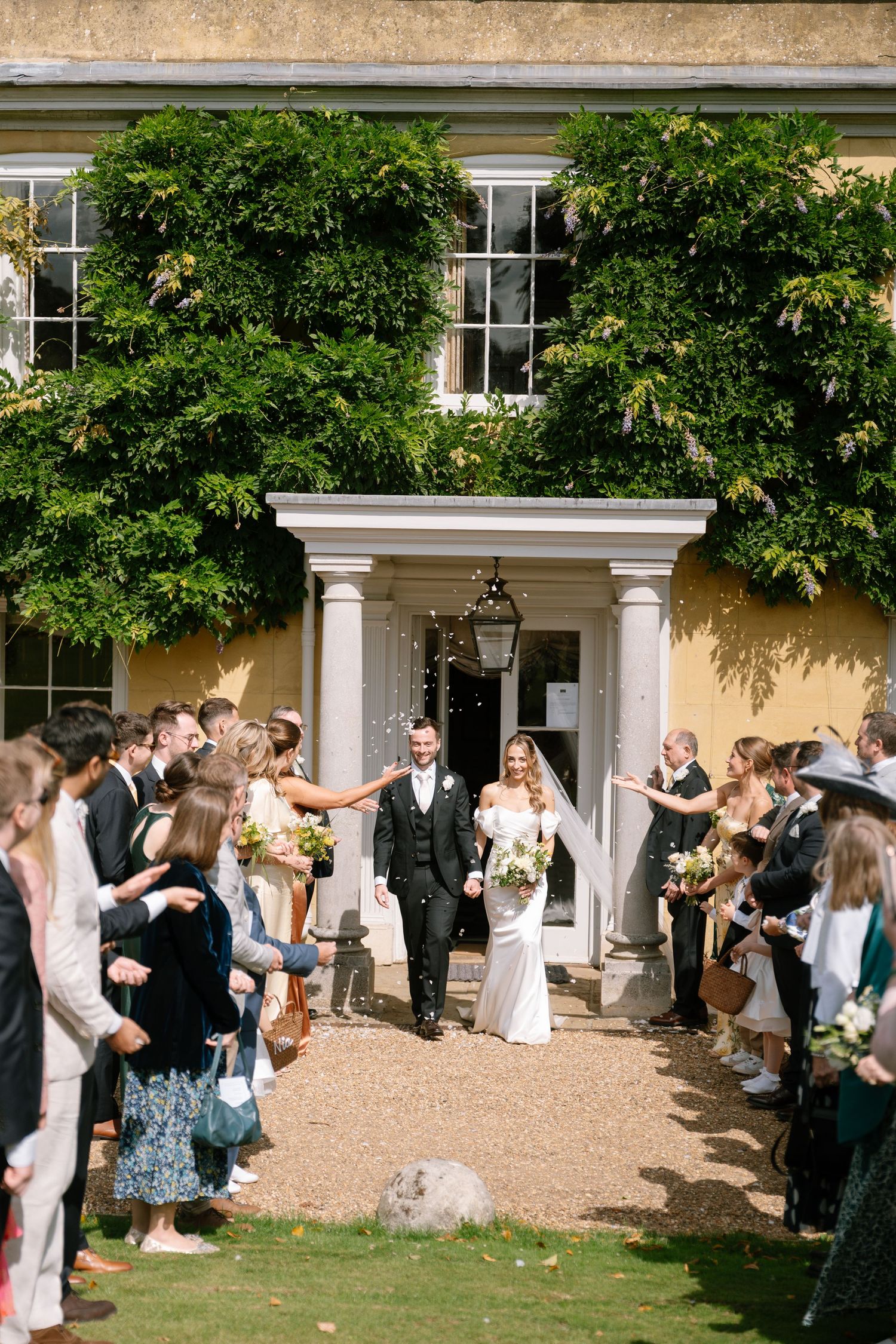 Wedding guests line up outside a yellow mansion for a celebratory moment.