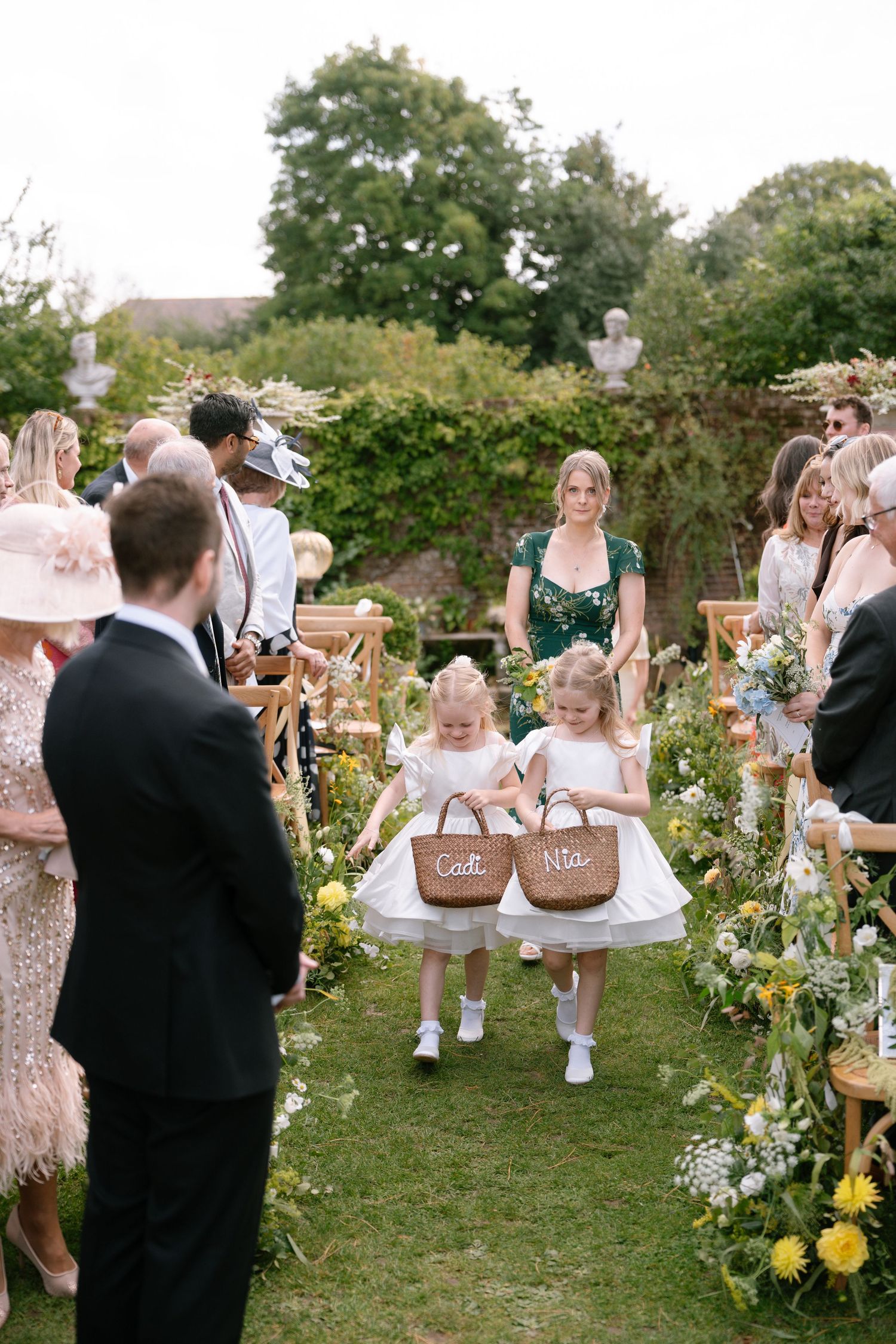 Wedding guests gather in a garden setting with yellow flowers and decorative chairs.