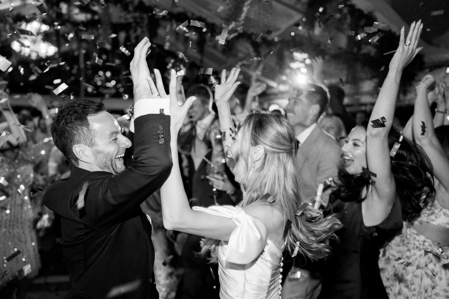 Wedding guests dancing and celebrating on a crowded dance floor with hands raised in the air.