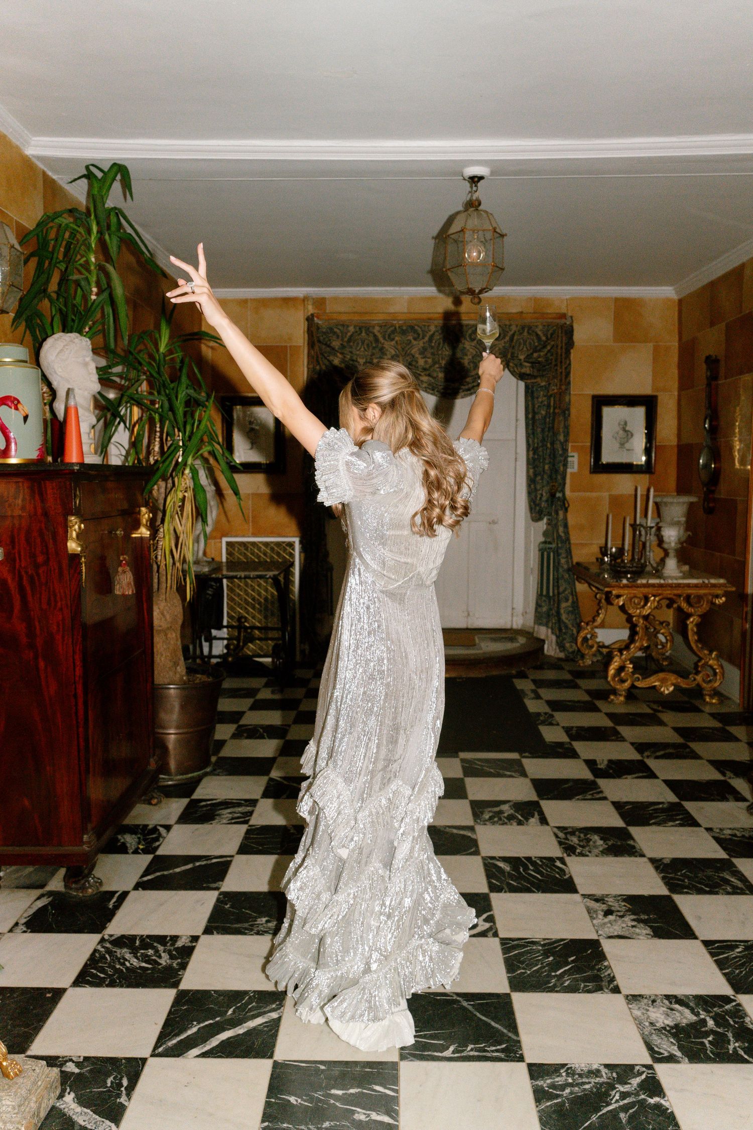 Someone in a glittering dress dances with raised arms on a black and white checkered floor.