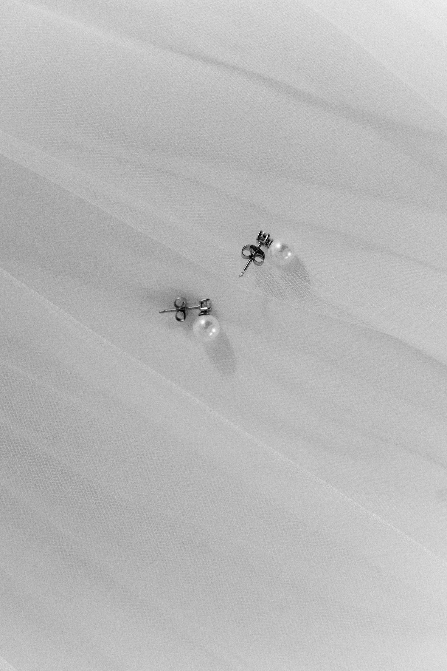 Pearl stud earrings on delicate white fabric in black and white photography.