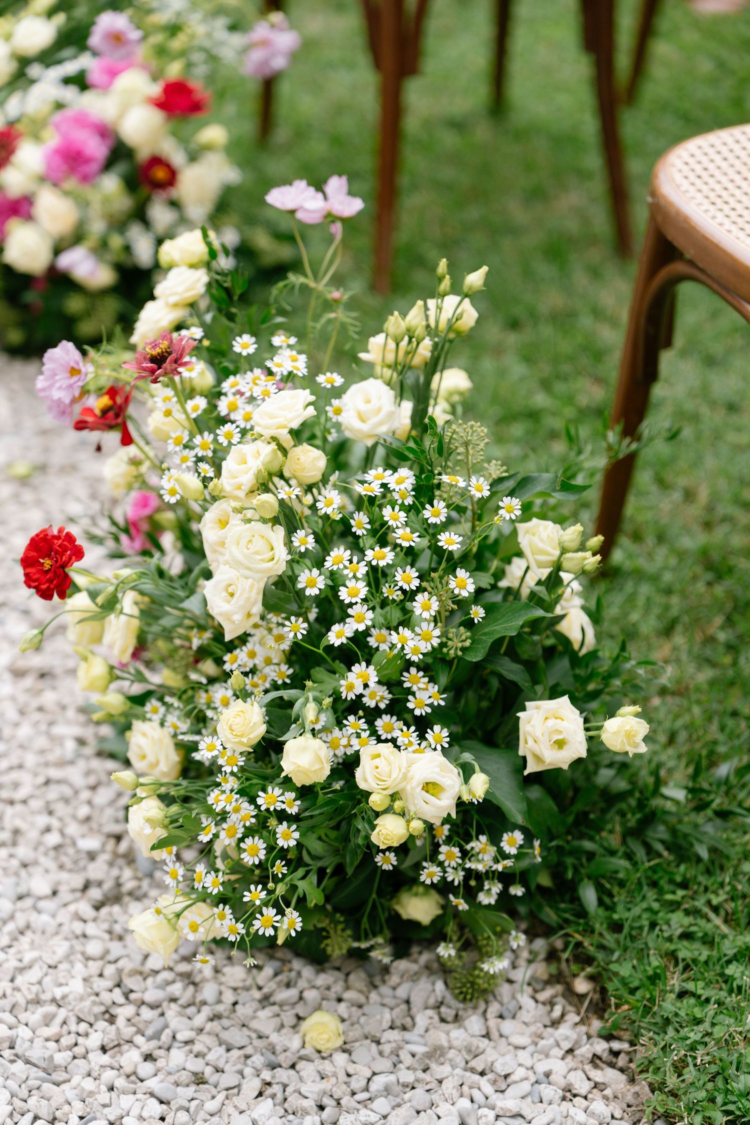 White and pink floral arrangements with daisies and roses line a gravel pathway.