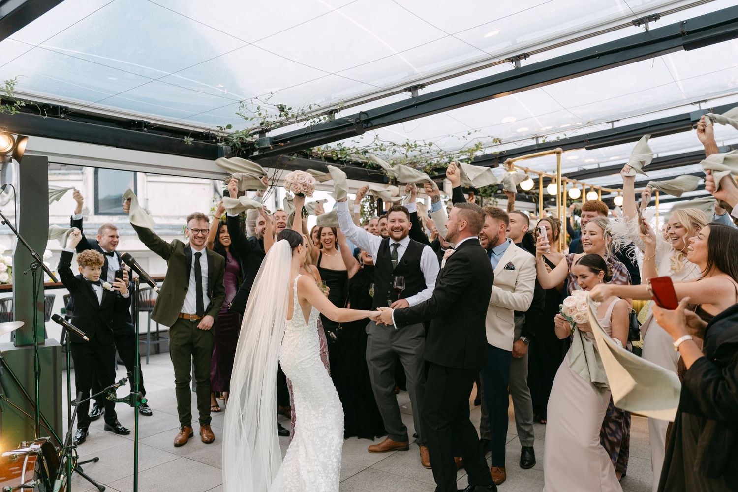 Wedding celebration with guests dancing and cheering under a covered outdoor venue.