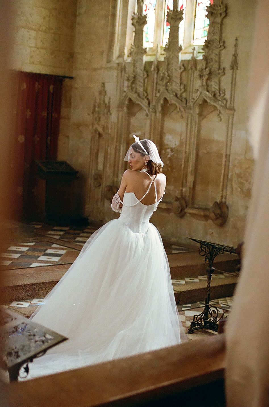 A bride in a flowing white gown twirls gracefully inside an ornate church with gothic architectural details.