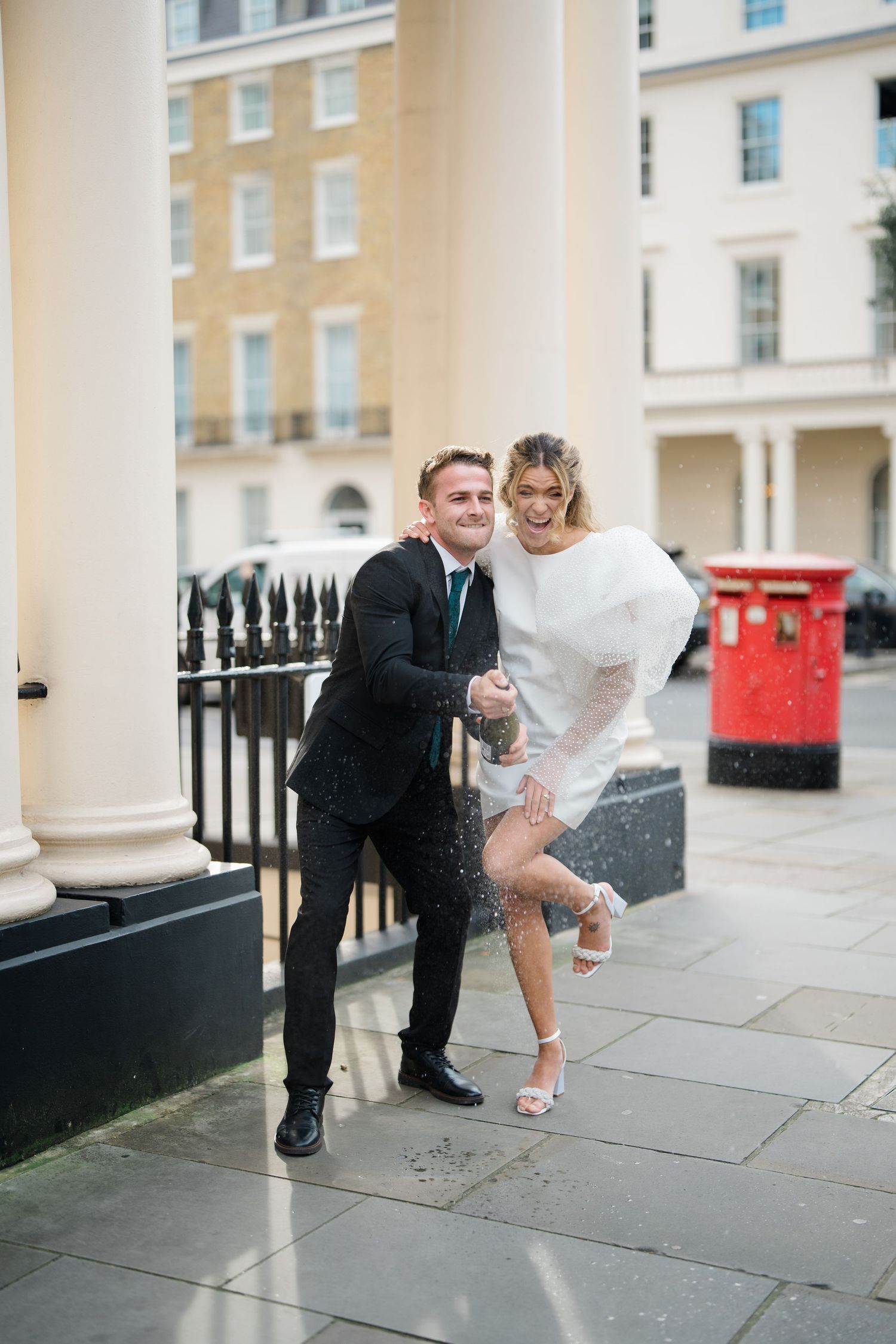 Candid moments of a couple dancing and laughing outside a historic building in London.