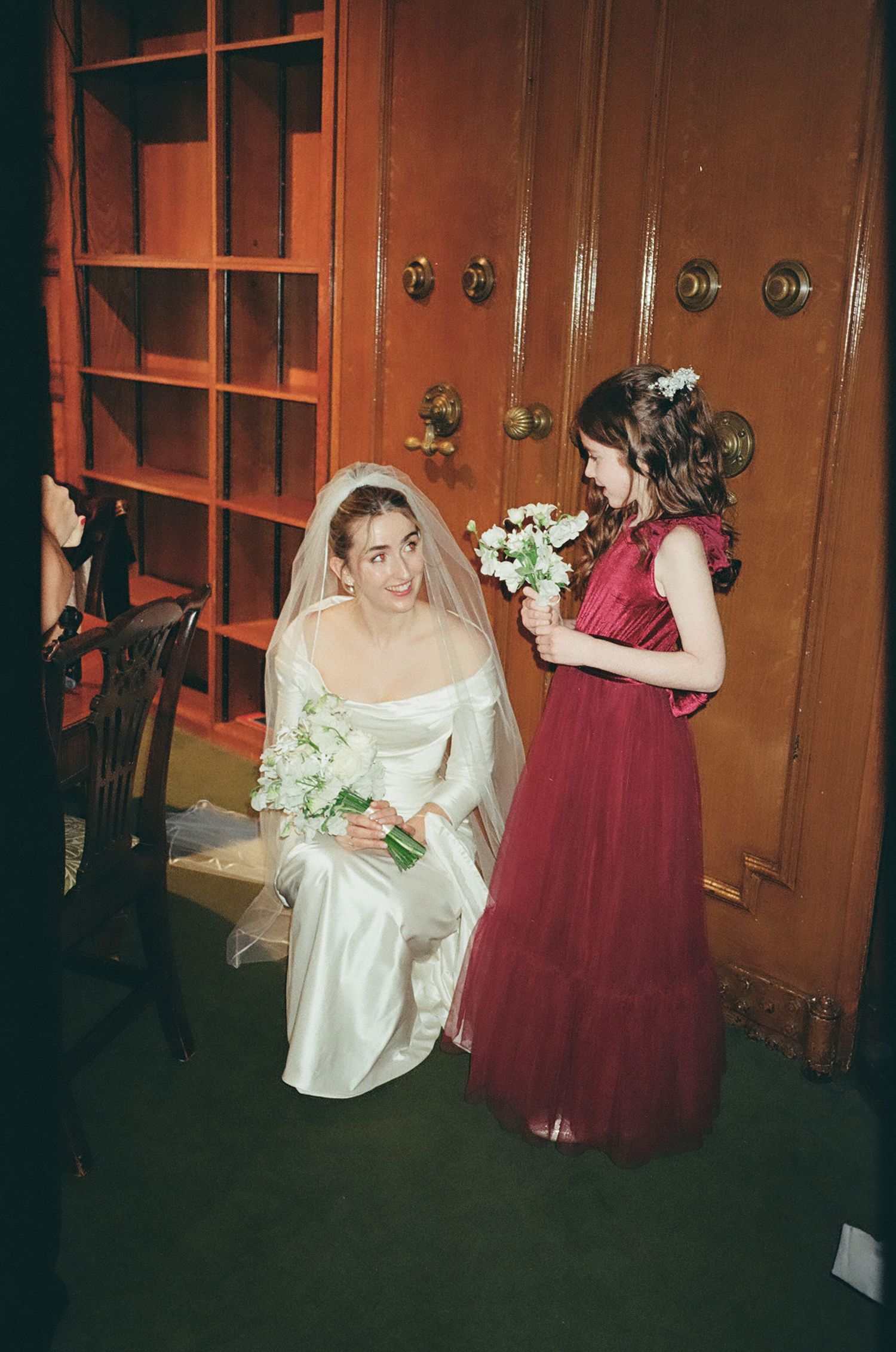 A wedding scene in a hallway with wooden doors and burgundy decor.