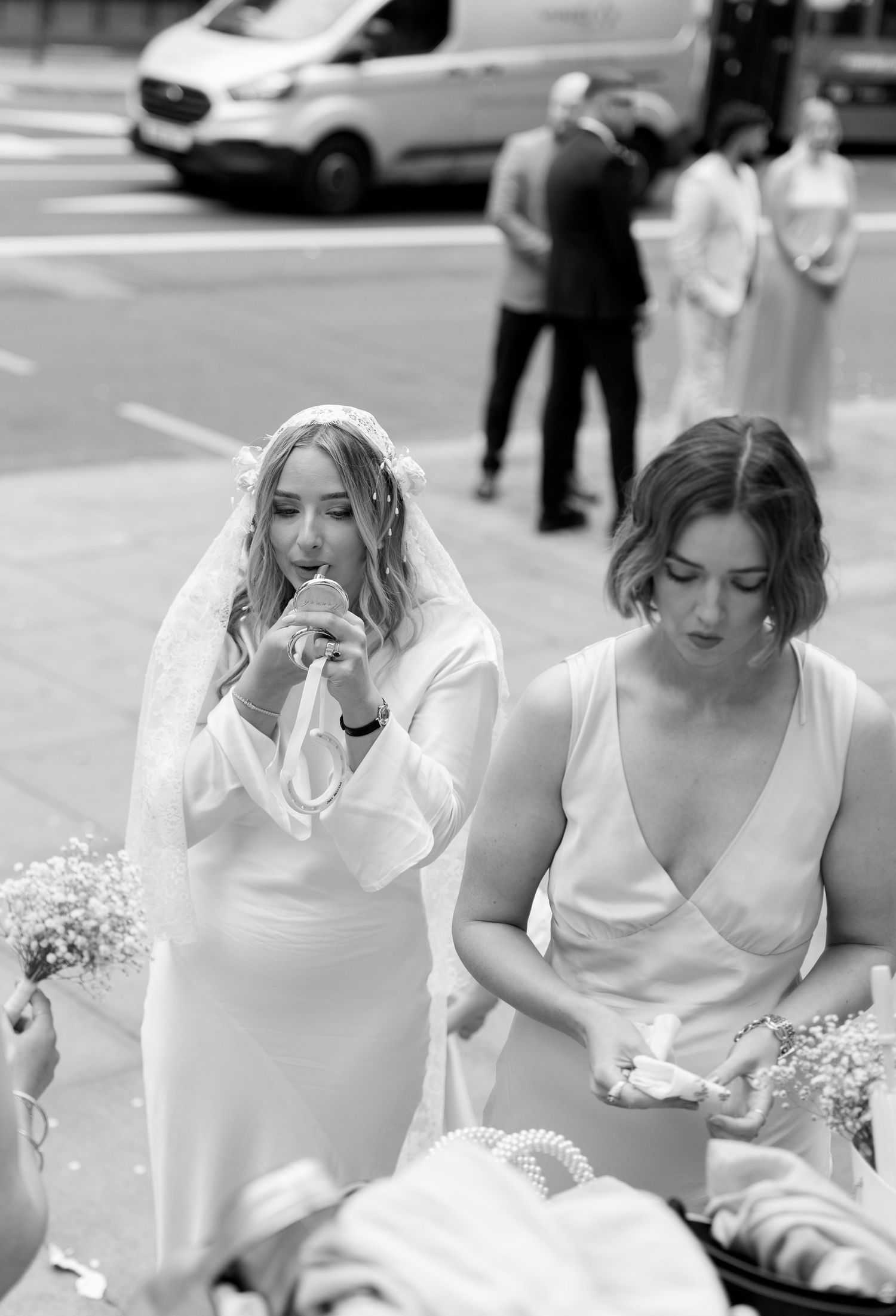 Wedding party in white dresses seated outdoors on a sunny day.