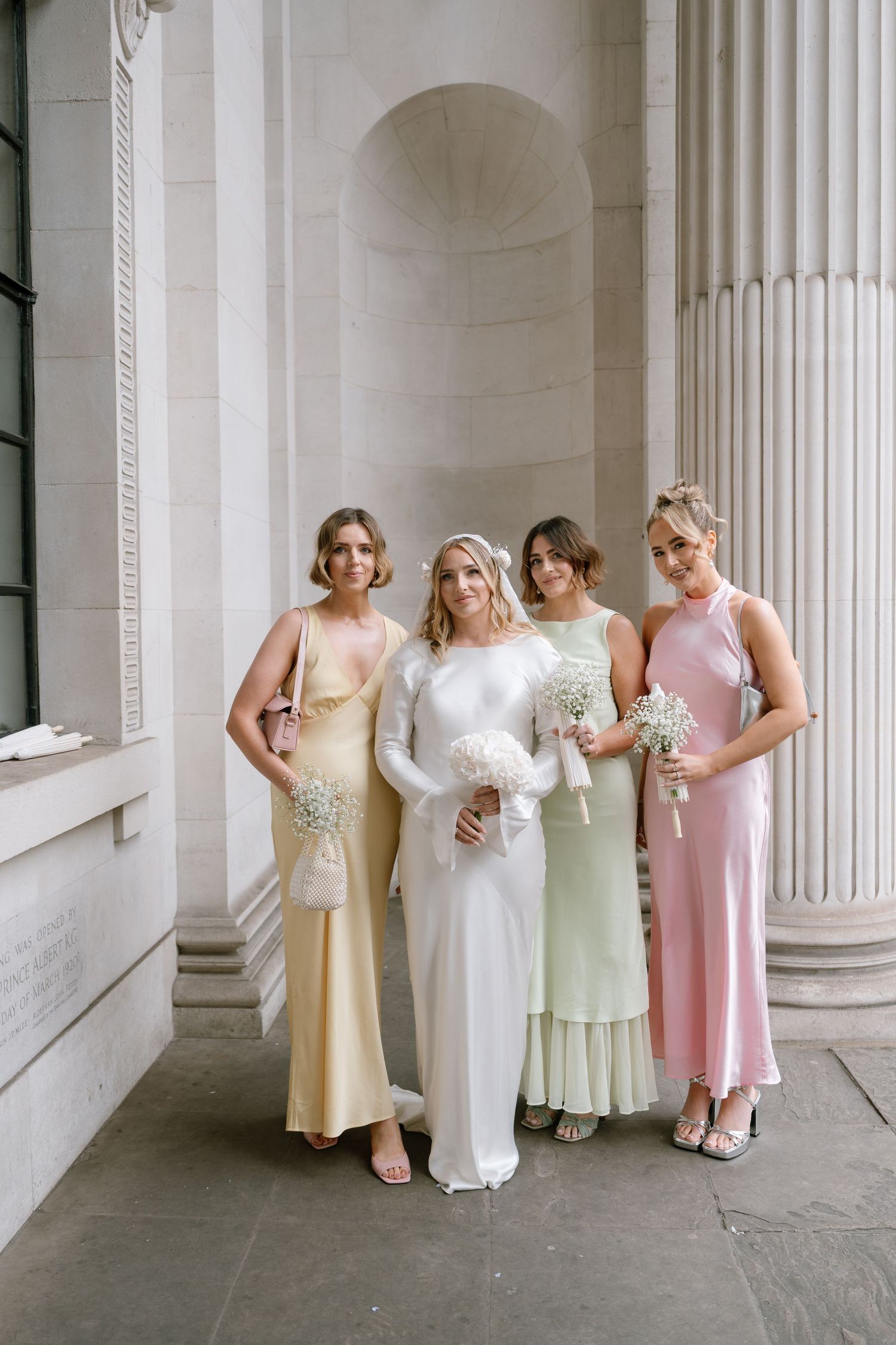 Wedding party in pastel dresses posing against classic white columned building.