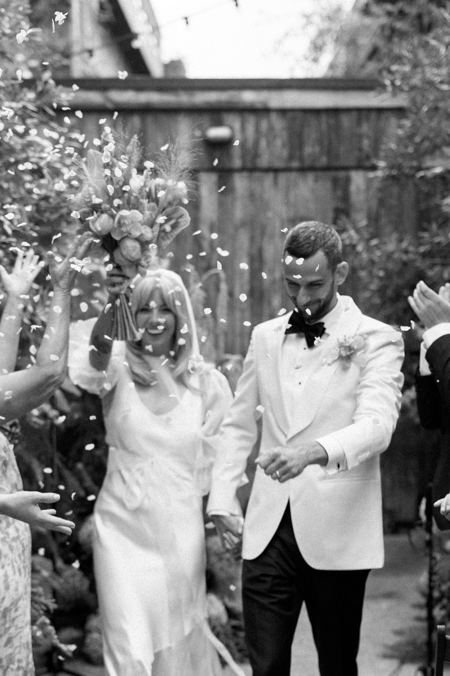 Wedding celebration with guests throwing confetti in a garden setting.