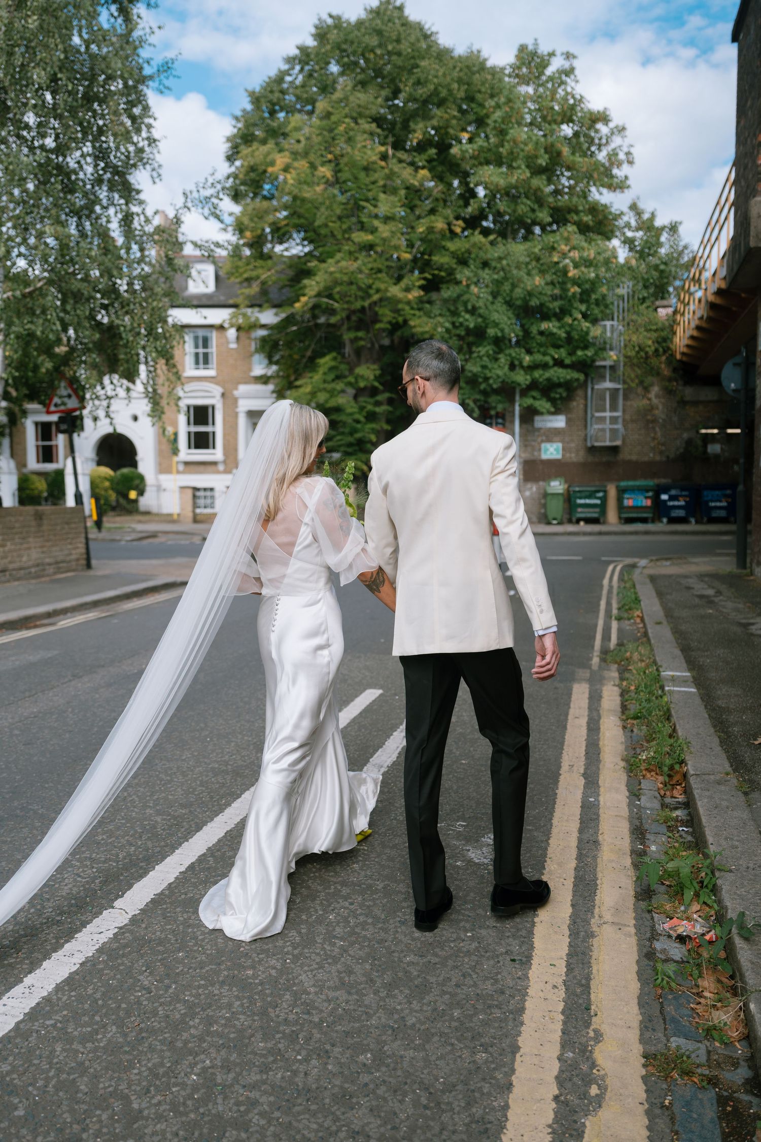 Wedding party walking down a tree-lined street in formal attire.