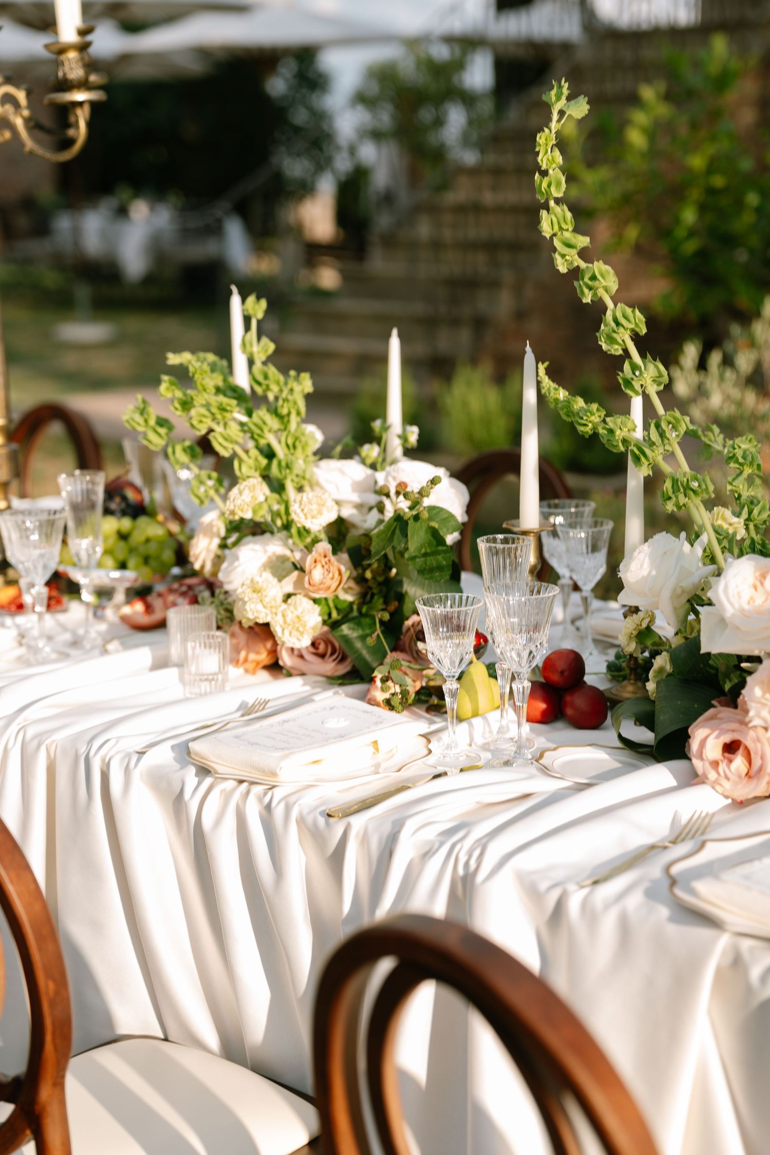 Elegant wedding table setting with white linens, candles, and floral centerpieces in soft pink and green.