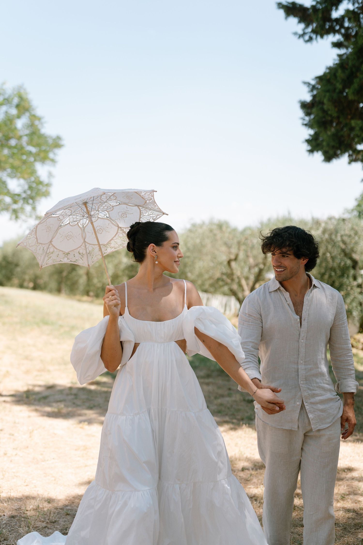 Outdoor portrait session featuring white parasols and light summer attire against a natural landscape.