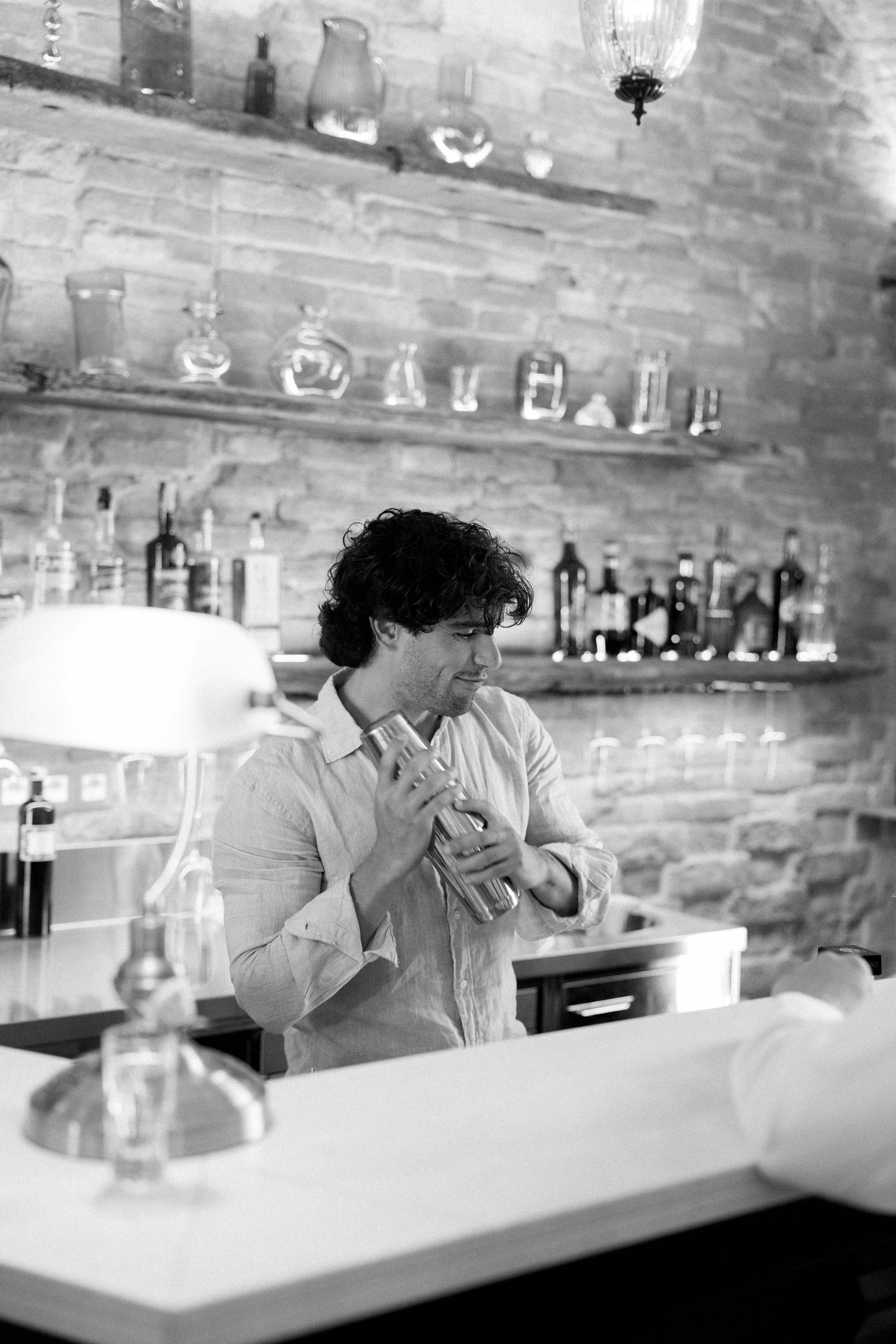Black and white sequence of someone sitting at a bar counter with glassware and bottles in the background.