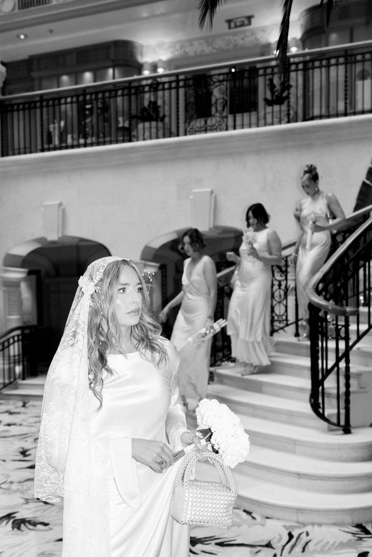 Wedding party descending elegant white marble staircase decorated with floral arrangements.
