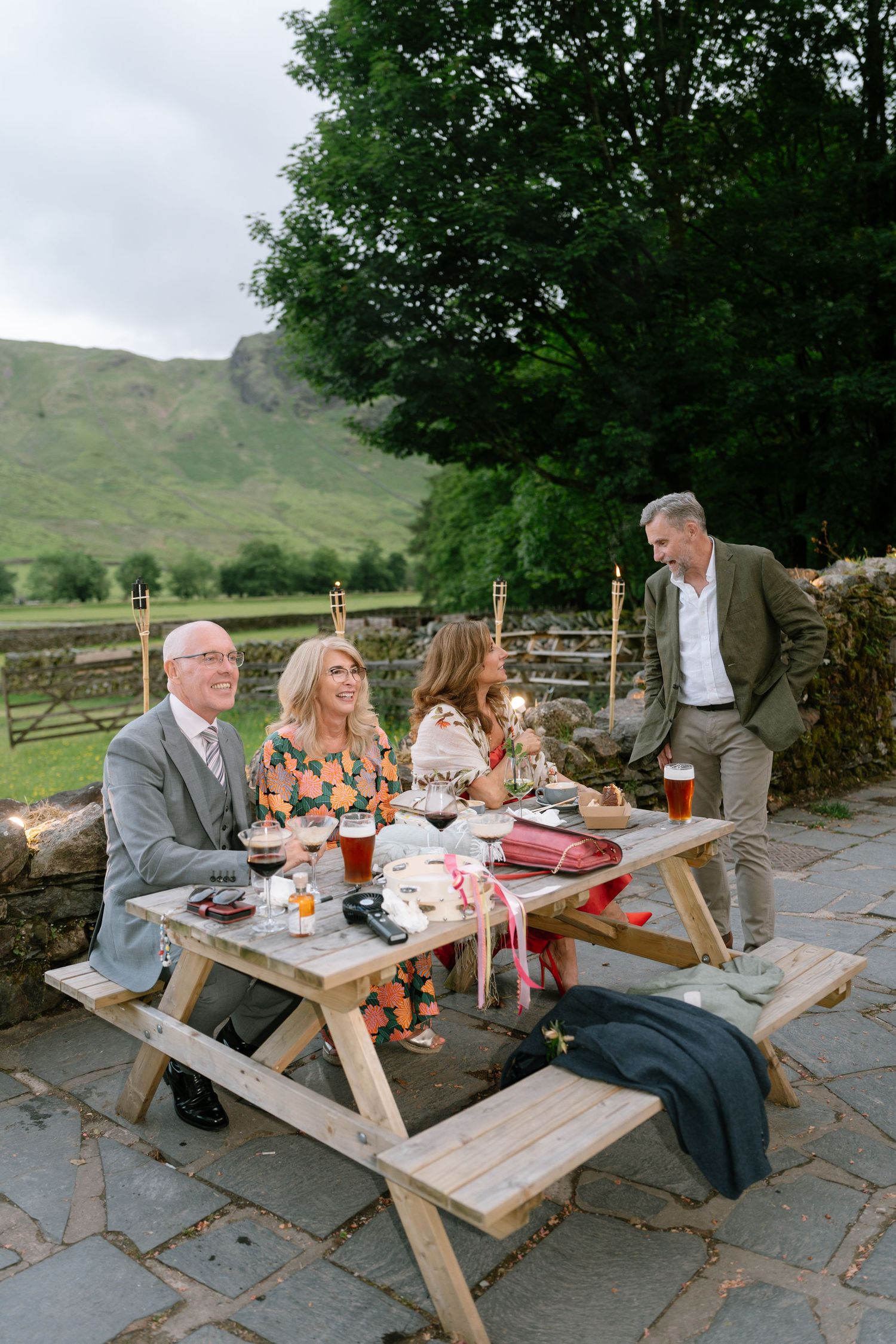Guests enjoying refreshments at wooden picnic tables during an outdoor reception.