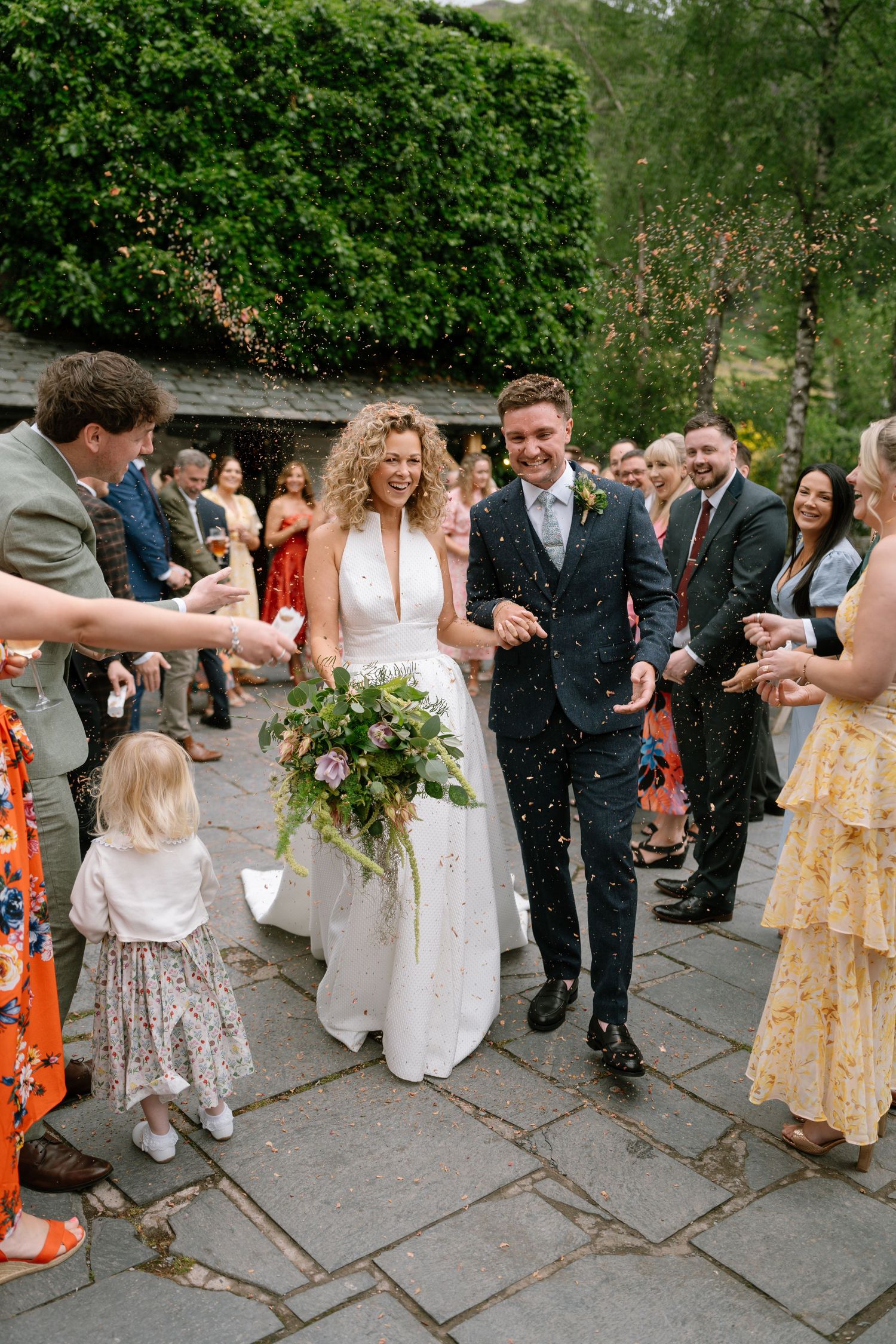 Wedding guests celebrate on a stone patio with confetti and bubbles during an outdoor reception.