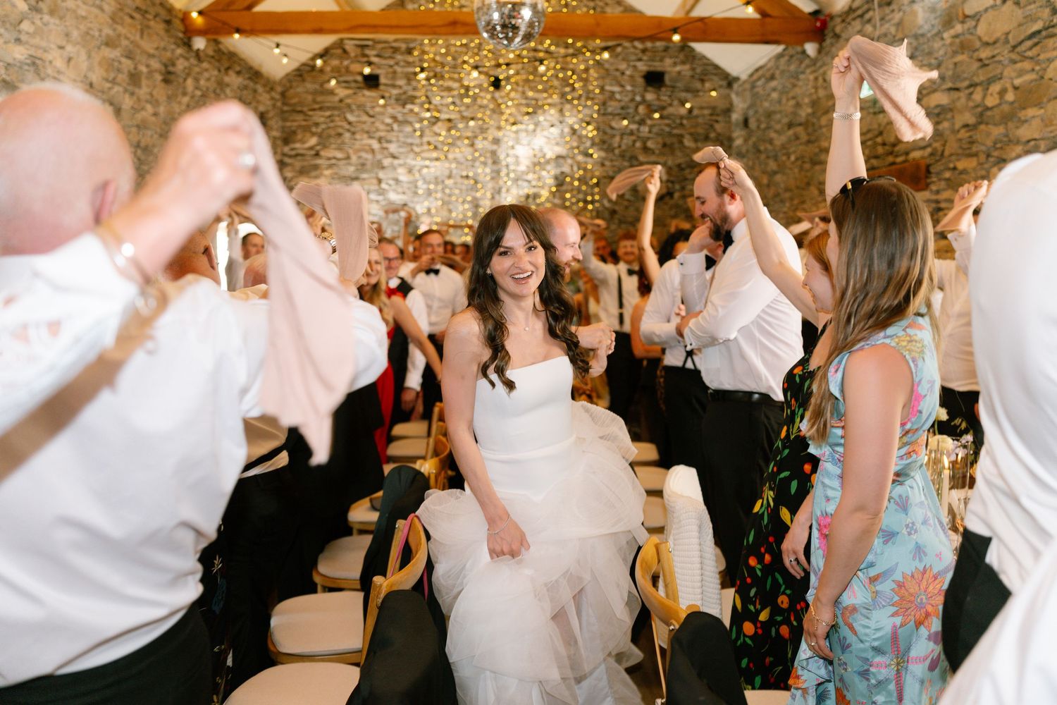 Wedding guests dancing and celebrating under string lights in stone venue.