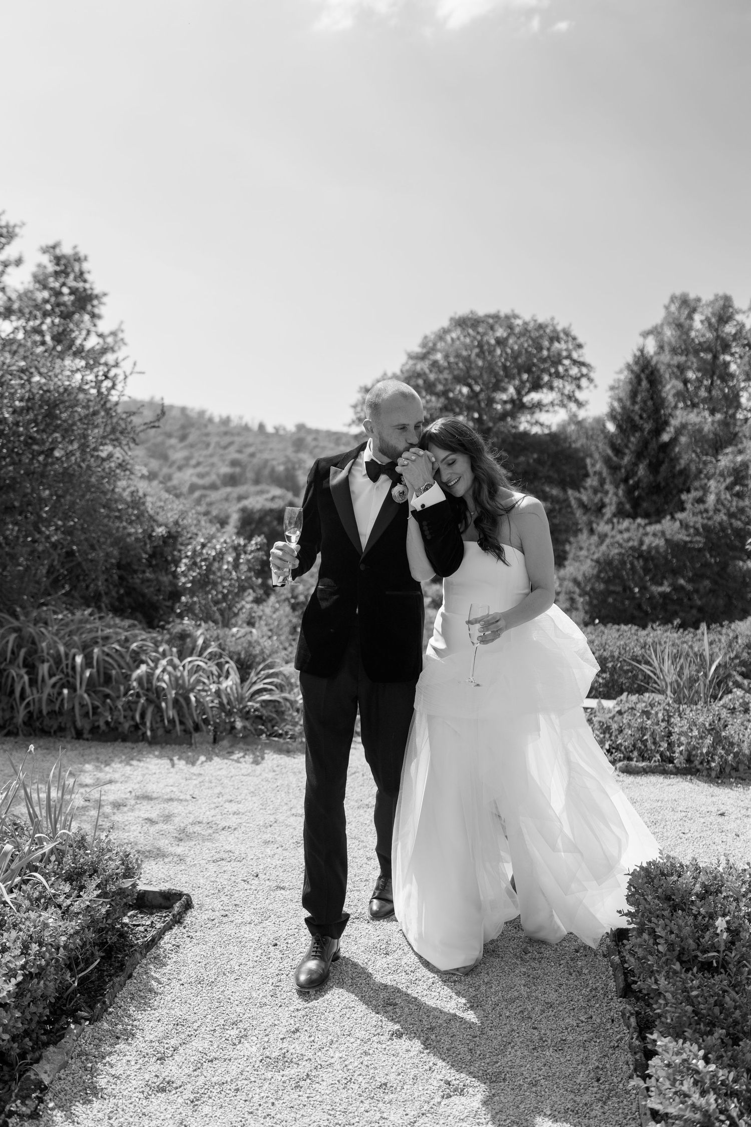 A series of wedding photos capturing a couple walking along a curved garden path surrounded by lush landscaping.