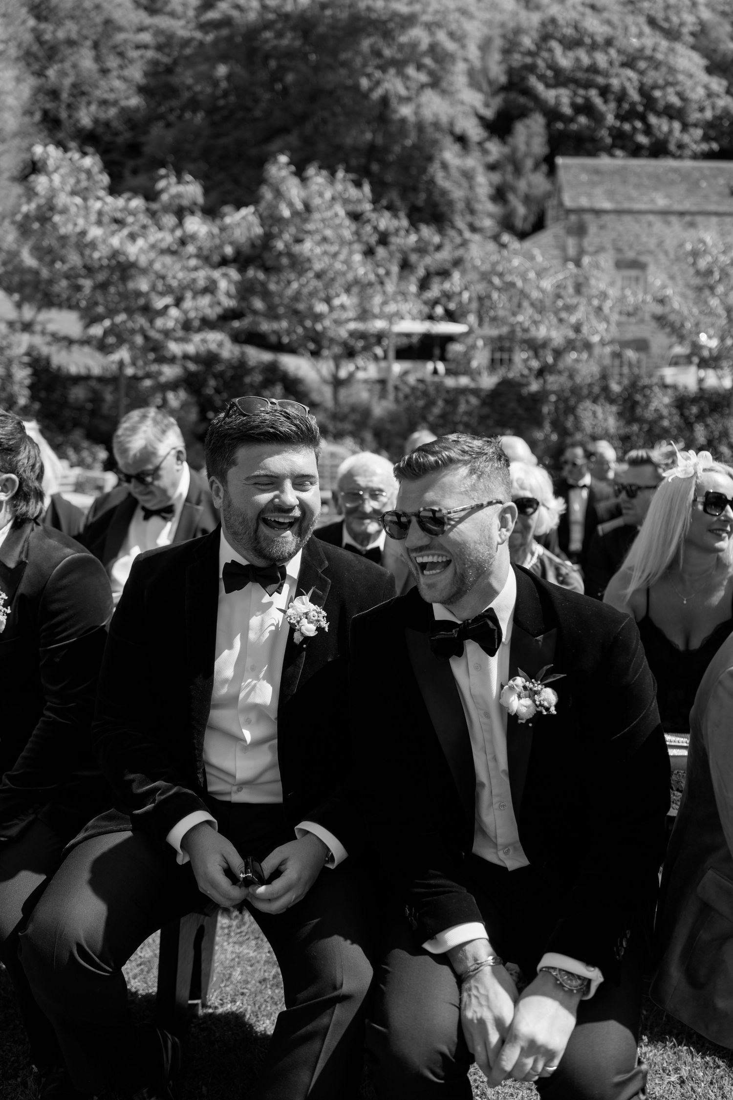 Guests in black tie attire share a laugh while seated outdoors.