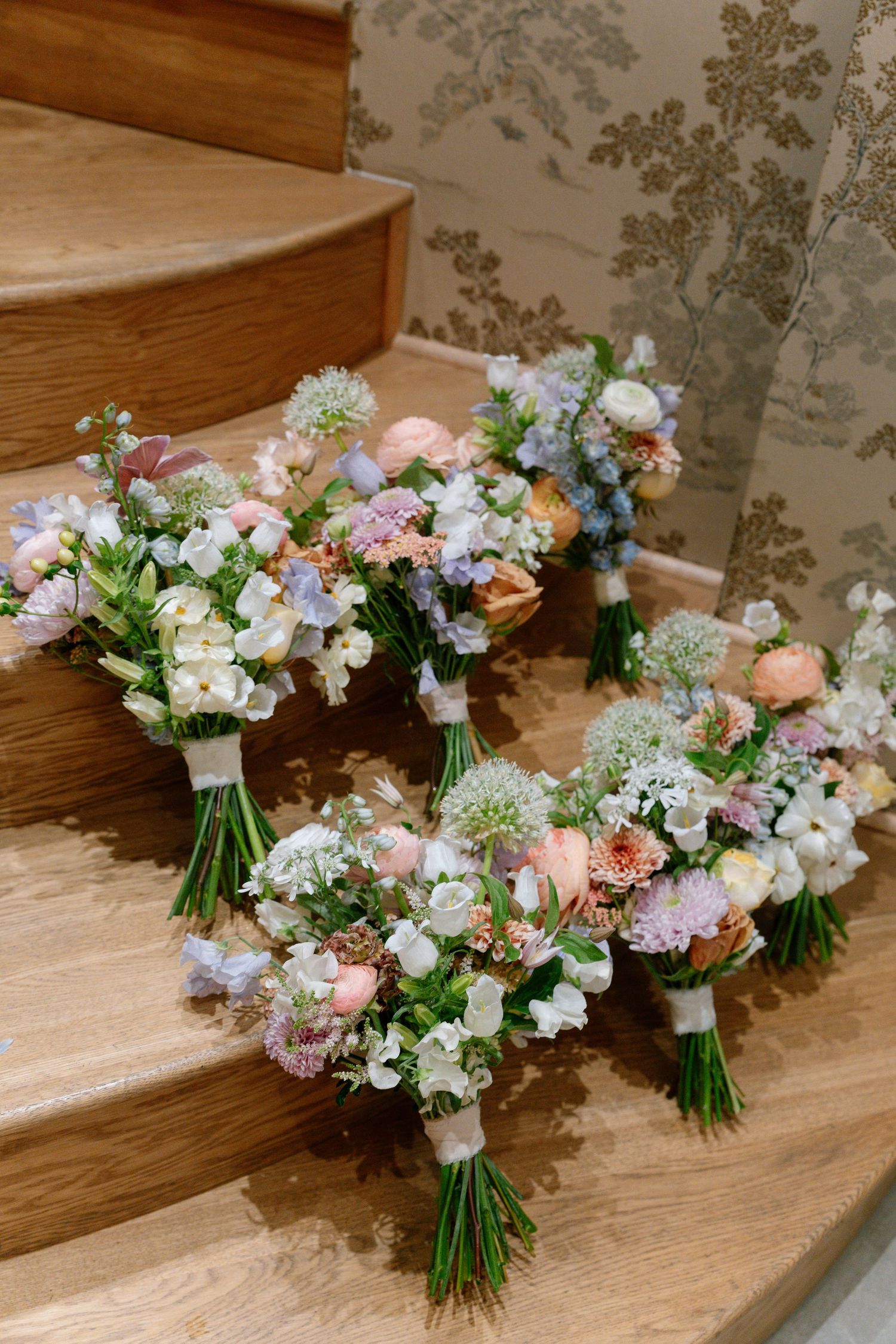 Delicate pastel wedding bouquets with roses and wildflowers arranged on wooden steps.