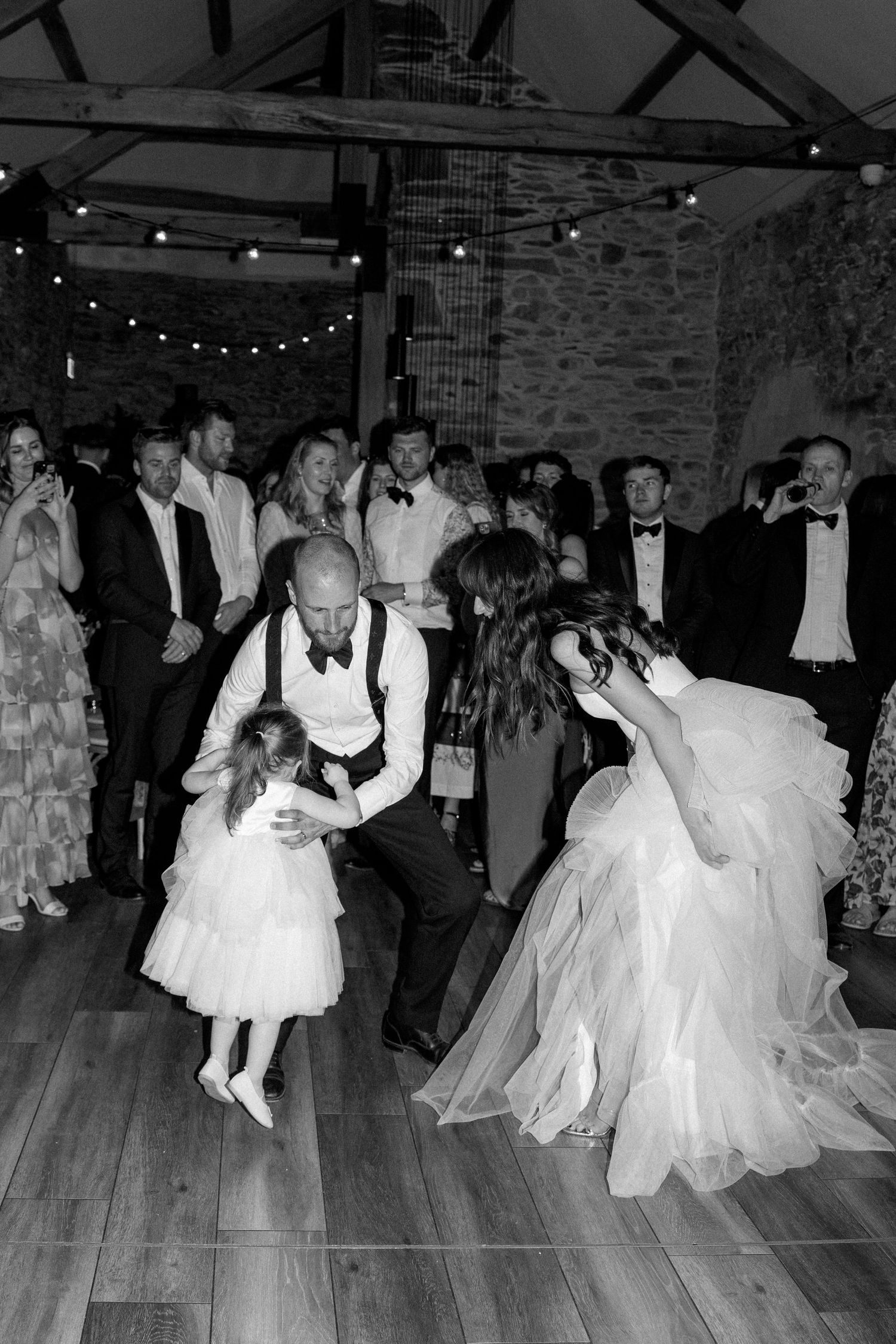 Couples dance together on a wooden floor during a wedding reception in a rustic venue.