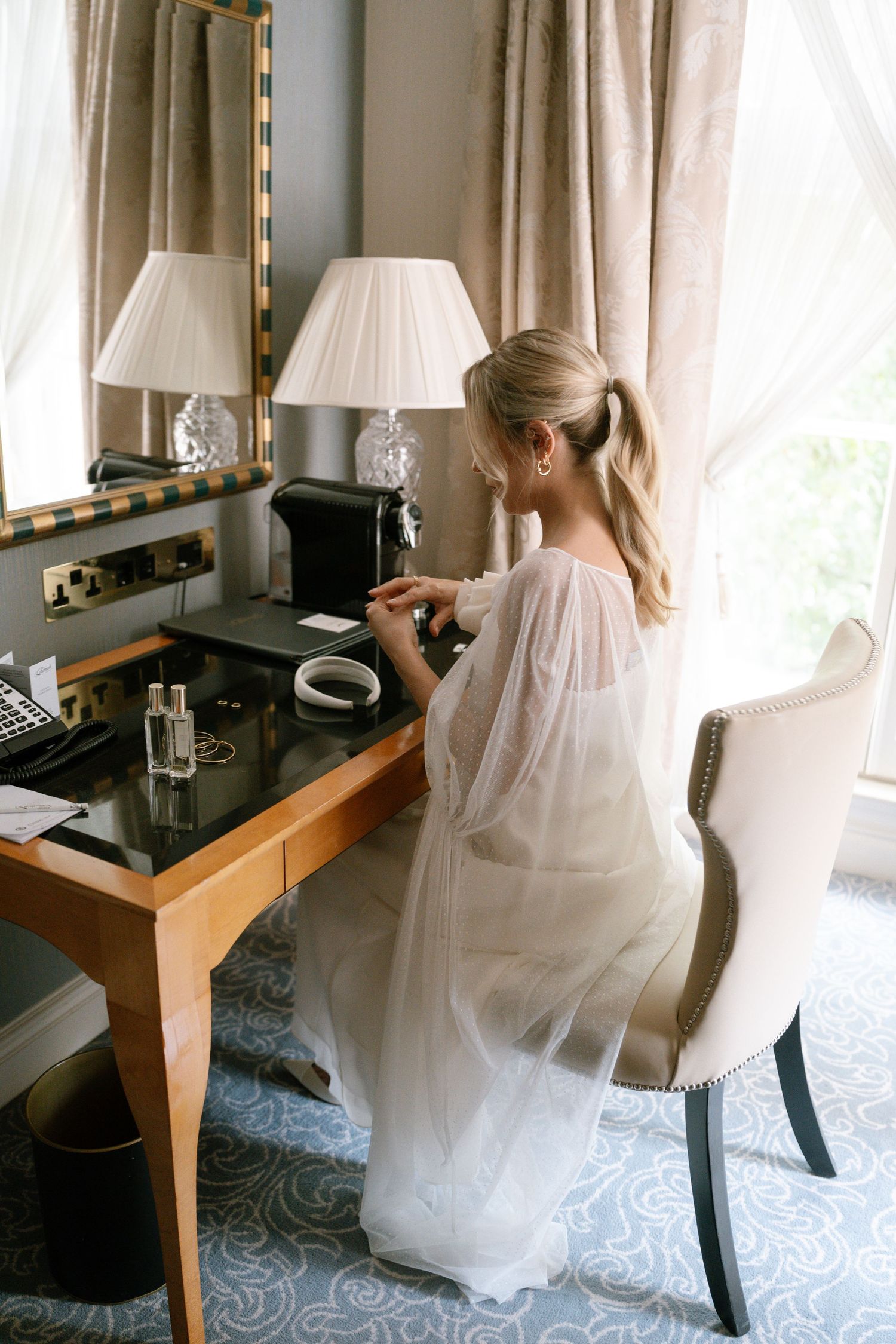 Bridal preparation scene at makeup vanity with elegant white robe and table lamps.