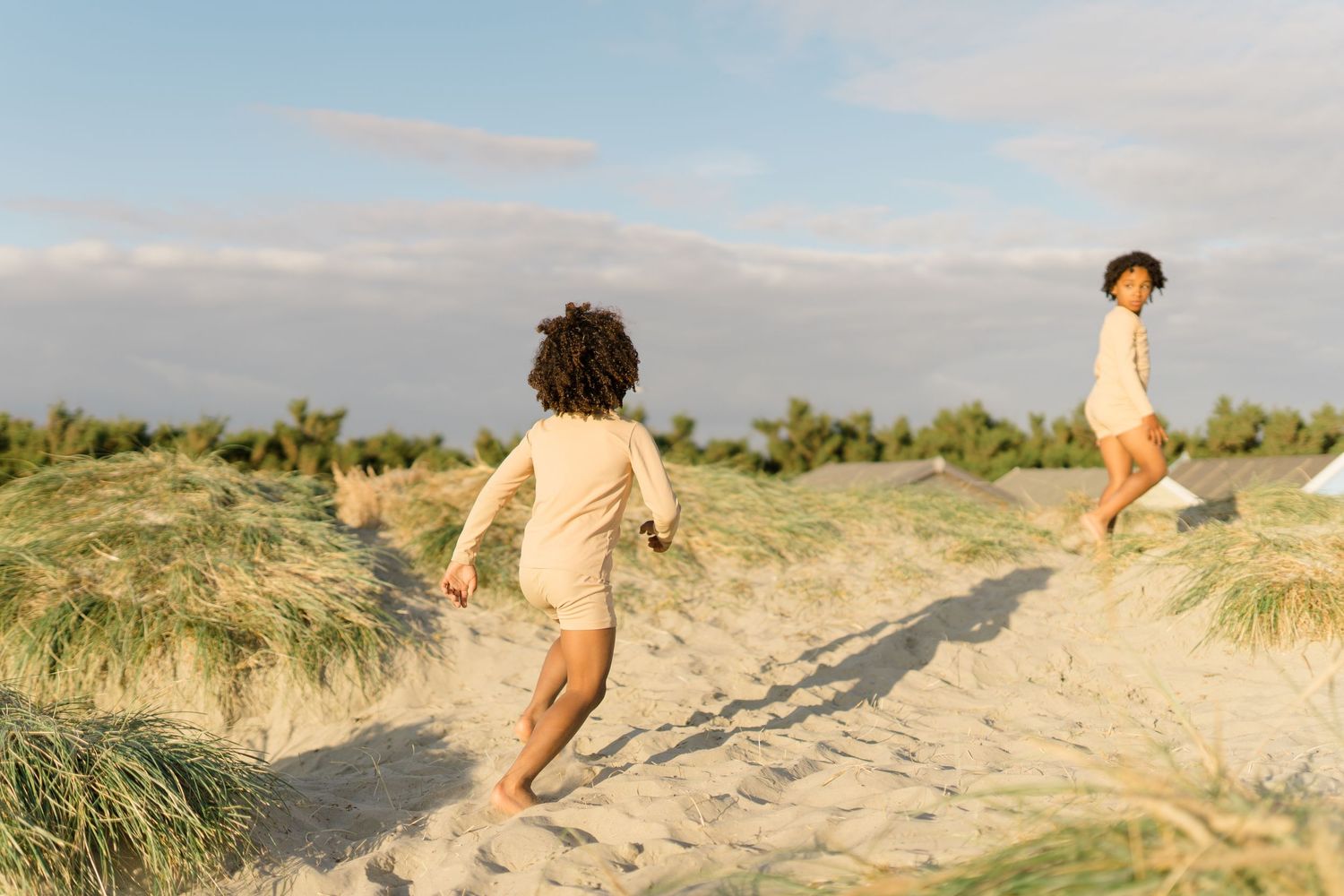 Figure running along sandy beach path surrounded by dune grass.