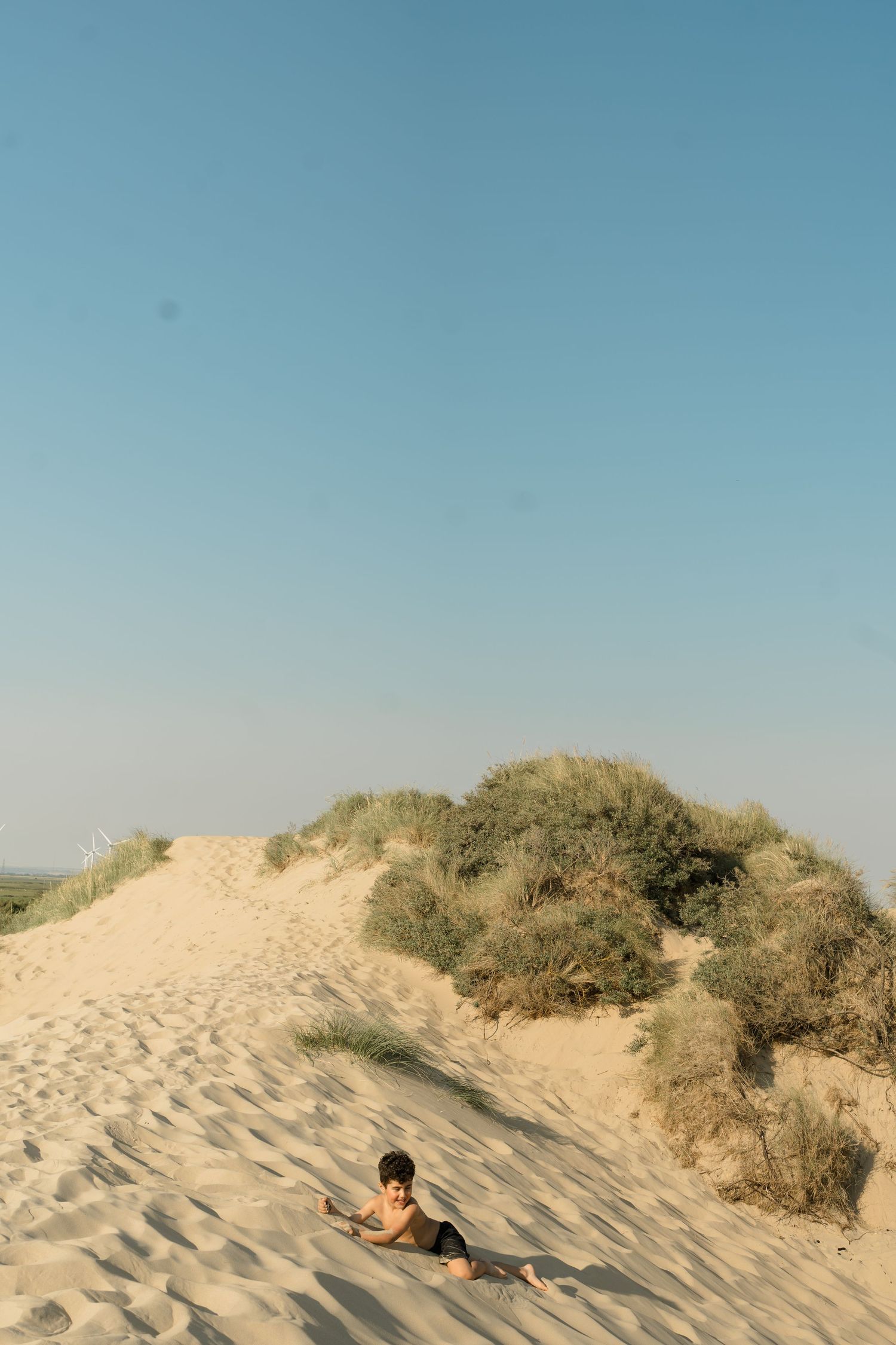 Person lying on sandy beach dunes with coastal vegetation in background.