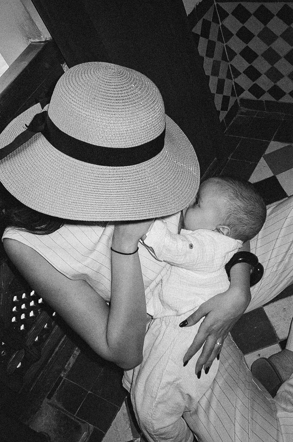 Black and white photo of a woman in a wide-brim straw hat tenderly kissing her baby.