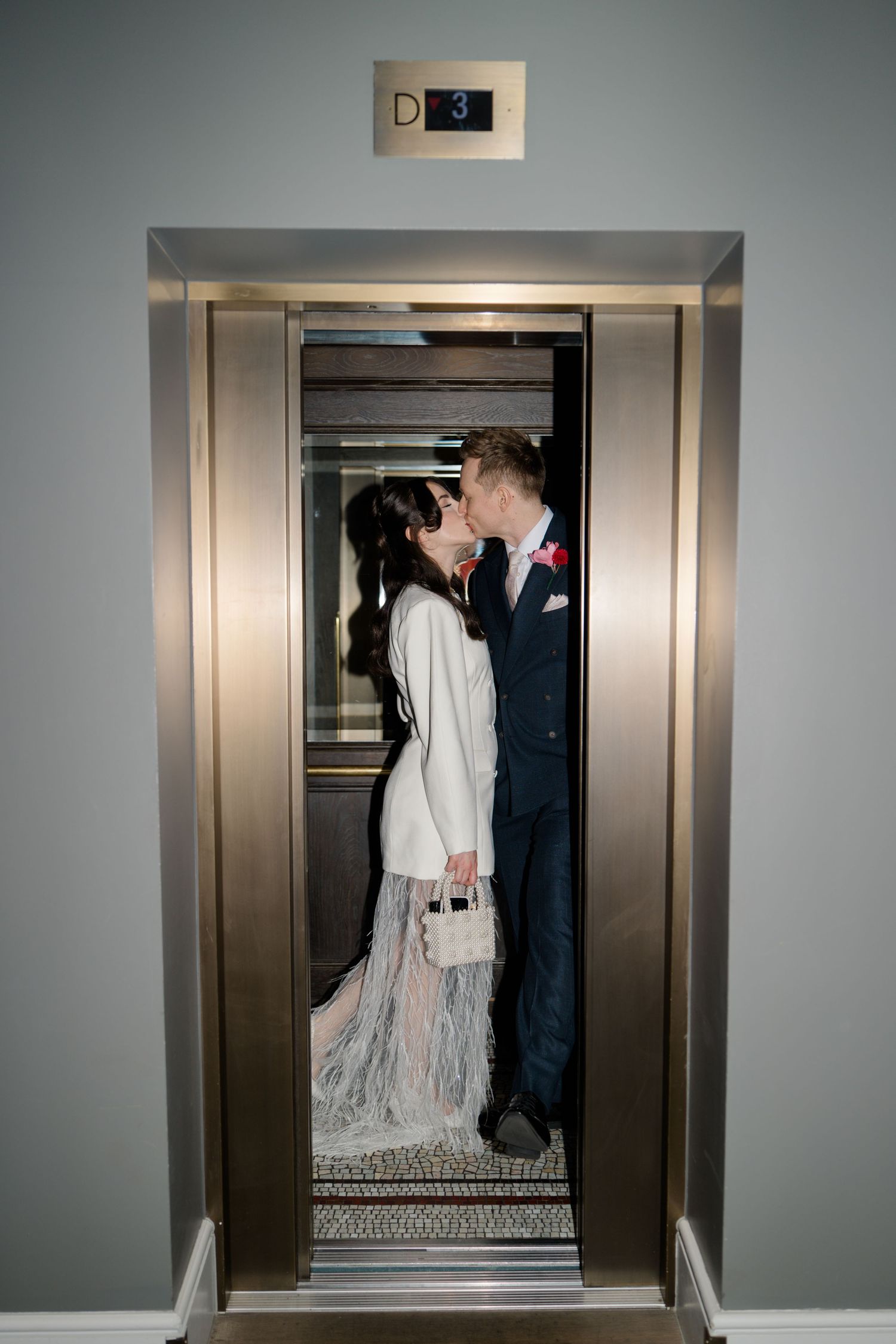 Bride and groom sharing a kiss inside a mirrored elevator on their wedding day.